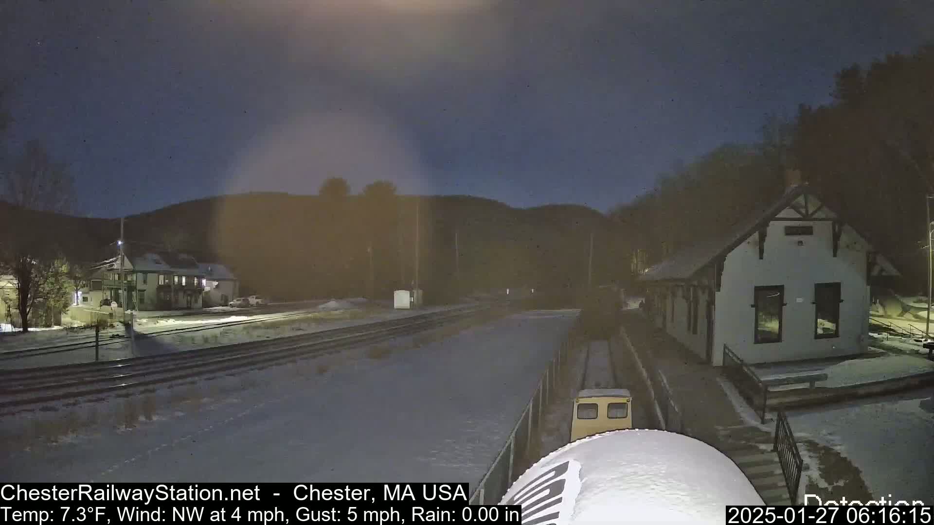 A snow-covered train station and tracks are visible at night under a dark, clear sky.