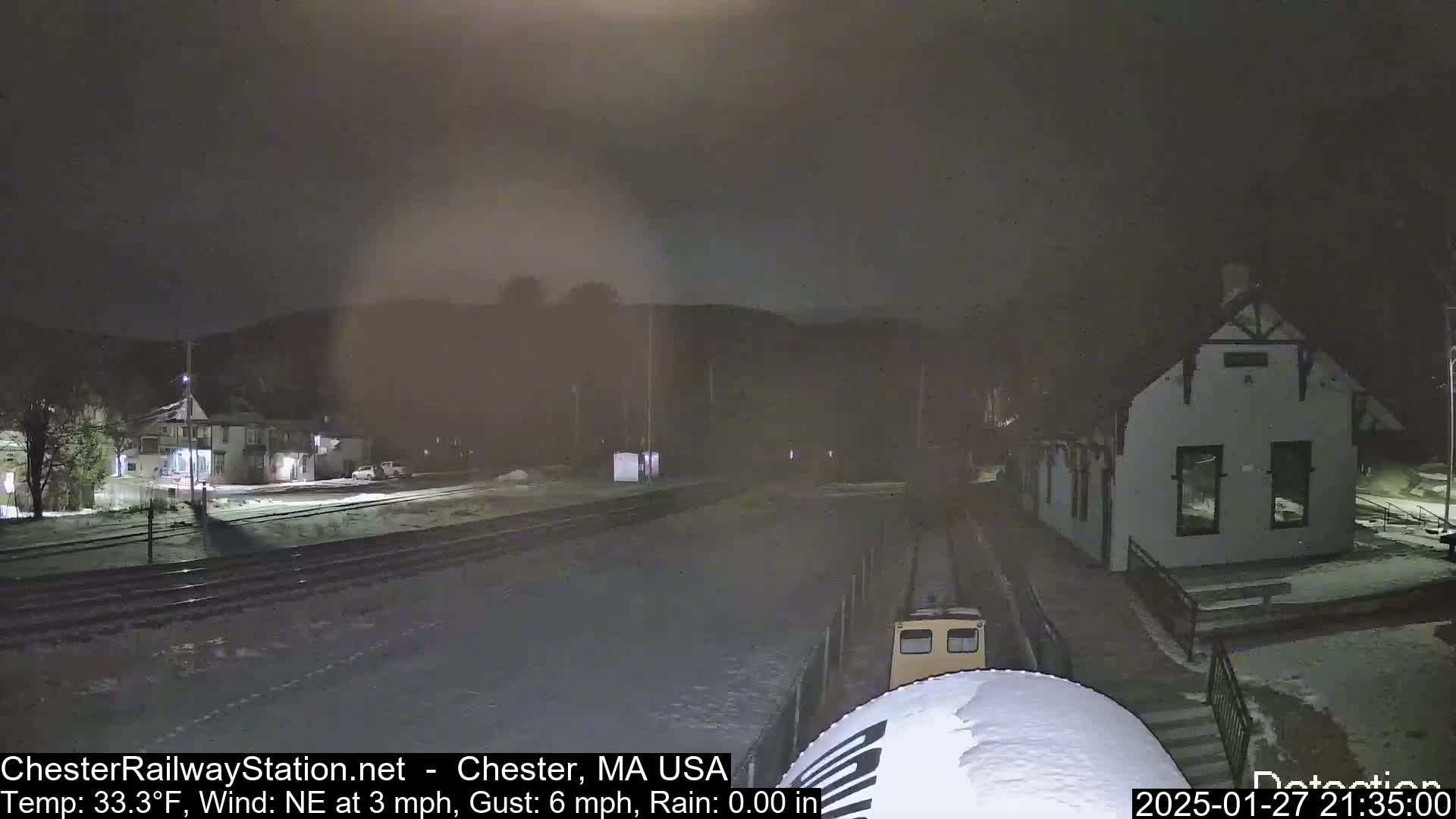 A nighttime view of a snow-covered train station and train car under a dark, overcast sky.