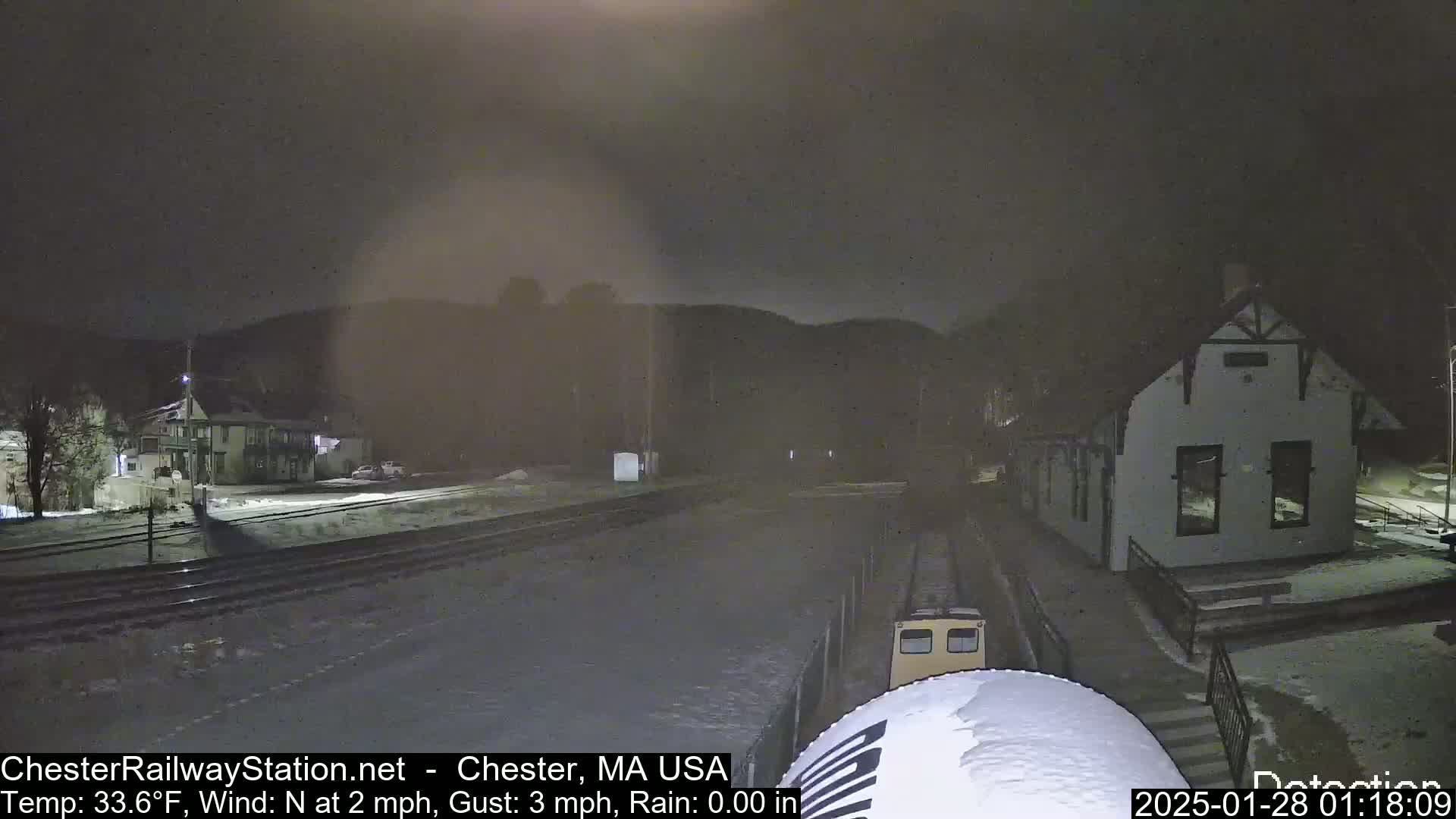 A train approaches a snow-covered train station at night under a dark, overcast sky.