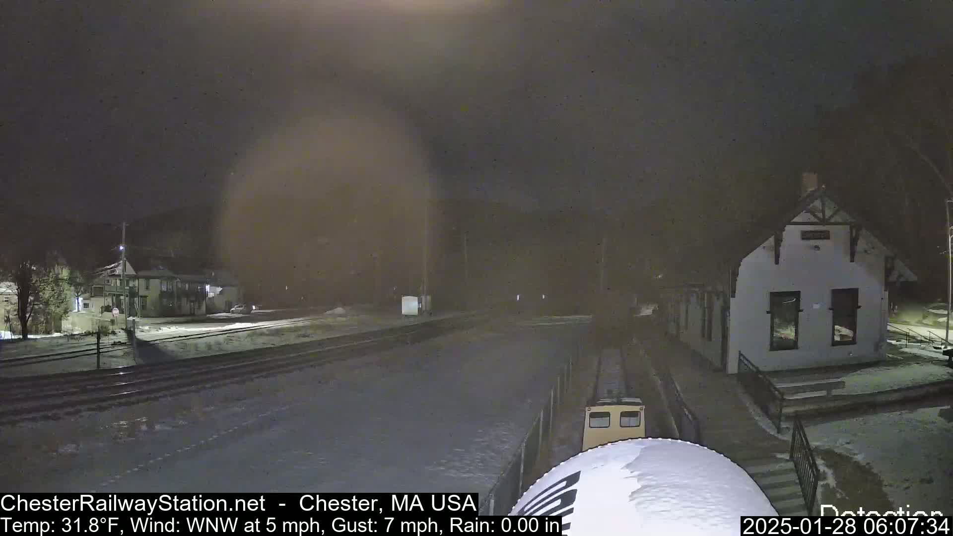 A small train sits in a snow-covered train station at night during light rain.