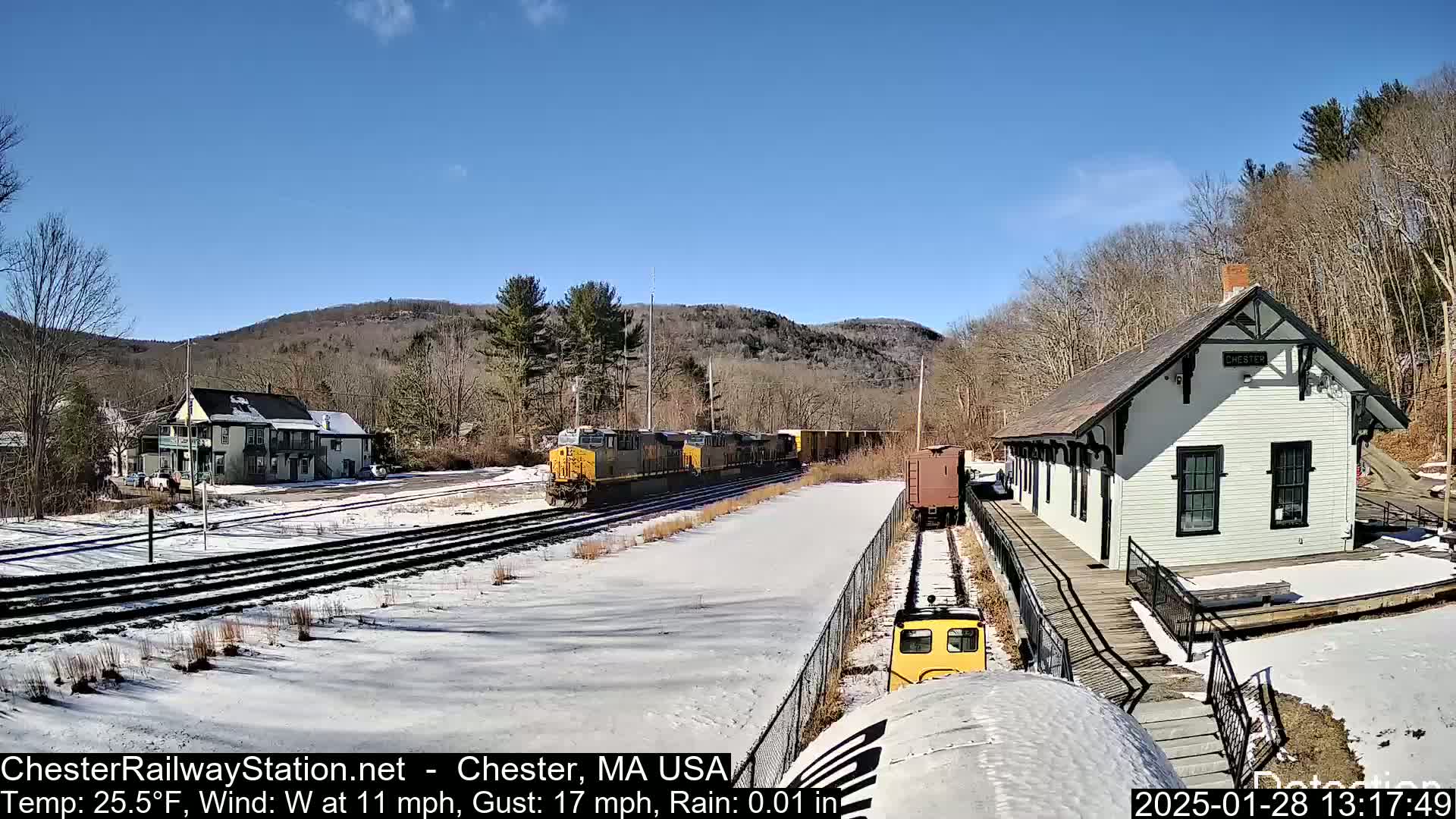A train passes a snow-covered railway station and small town under a sunny sky.