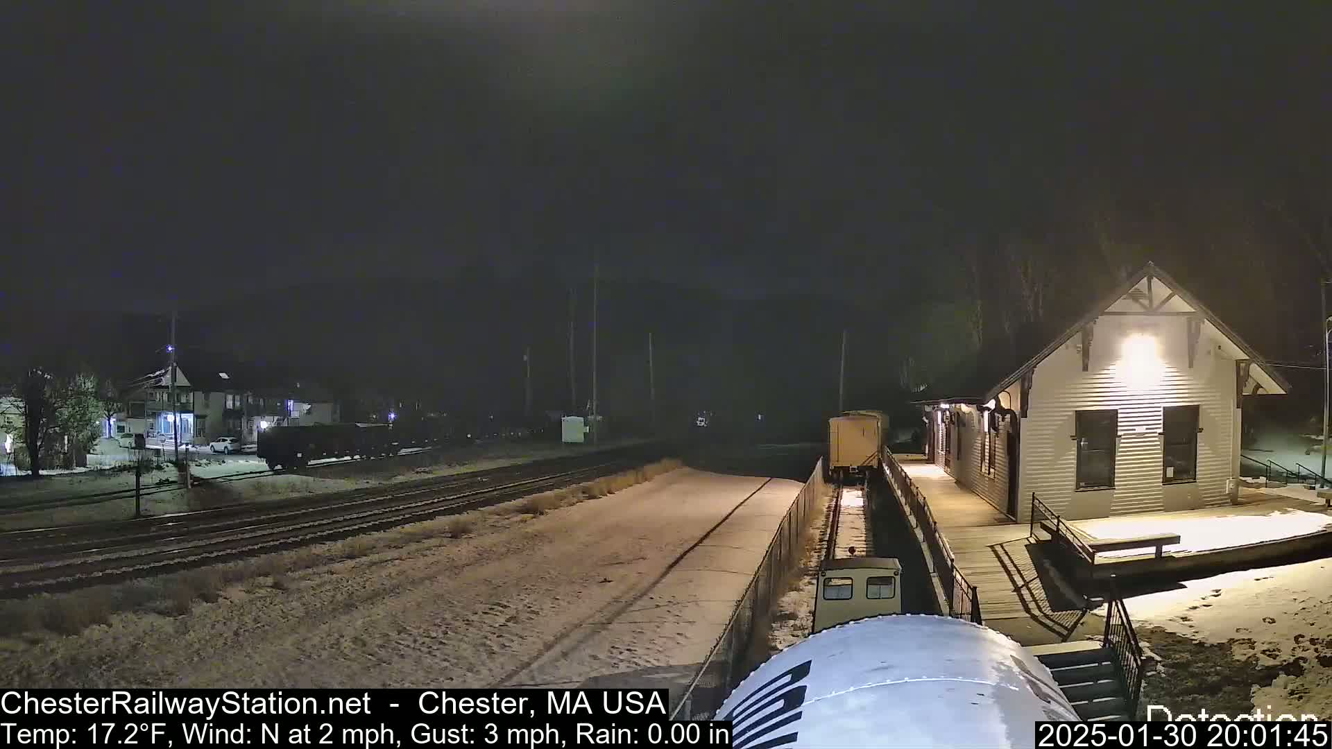 A nighttime scene shows a train approaching a snow-covered train station under a dark sky.