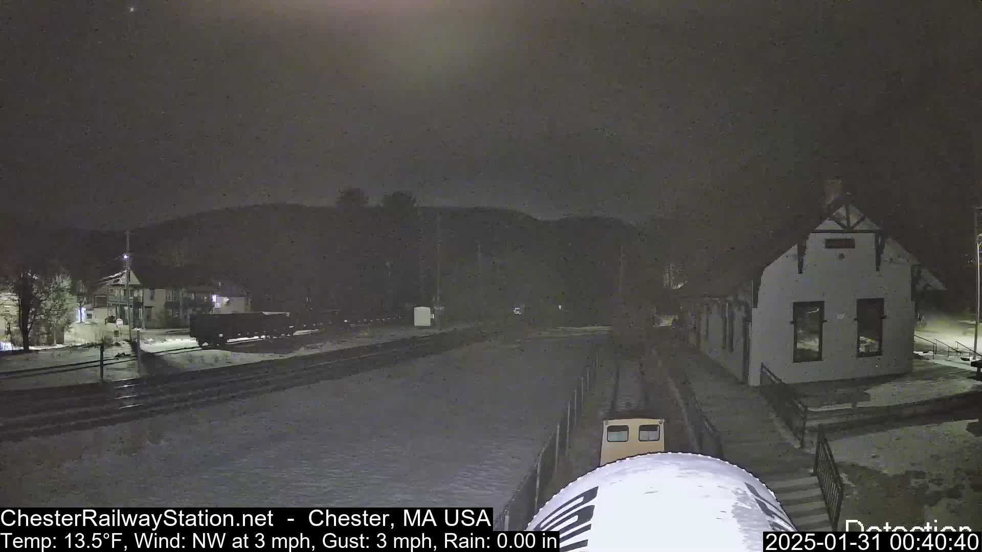 A snow-covered train station at night, with a train car partially visible in the foreground, under a dark, clear sky.