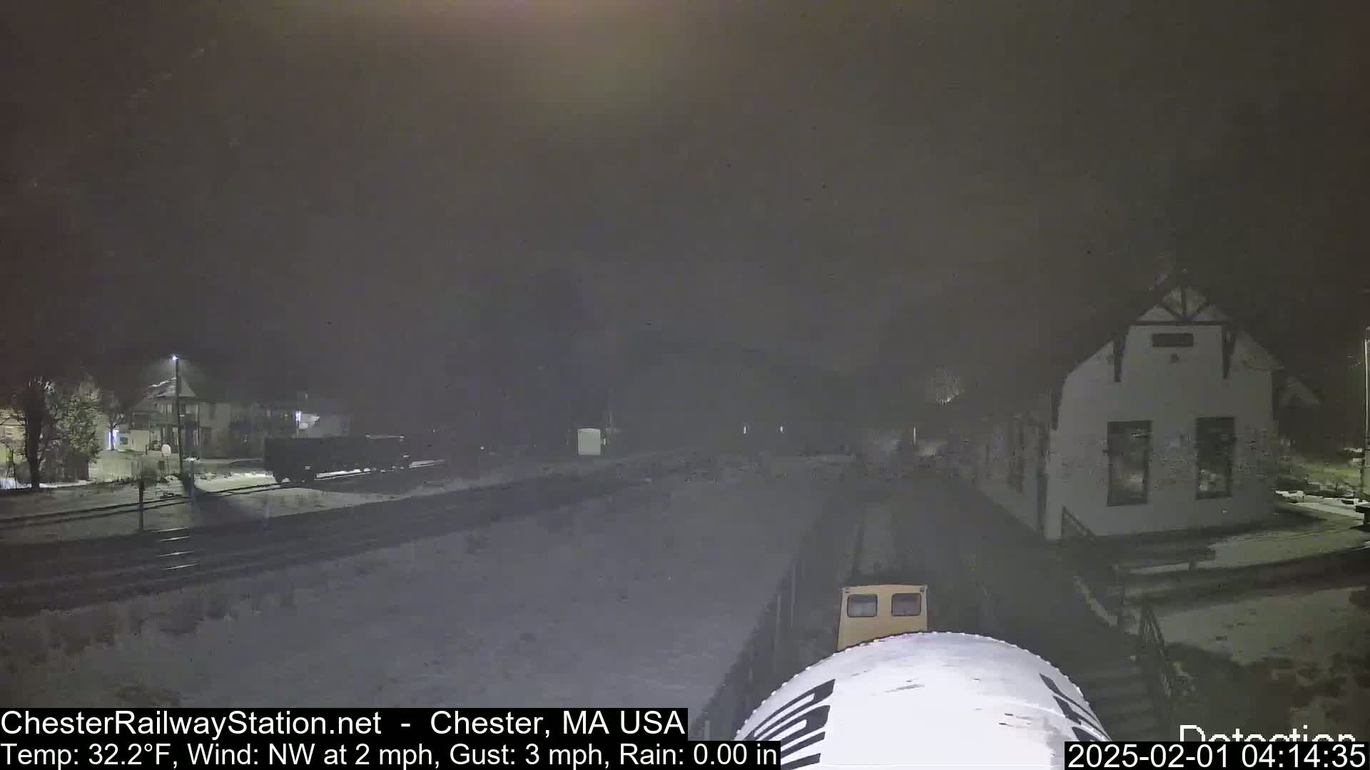 A nighttime view of a train partially obscuring a small building in snowy conditions.