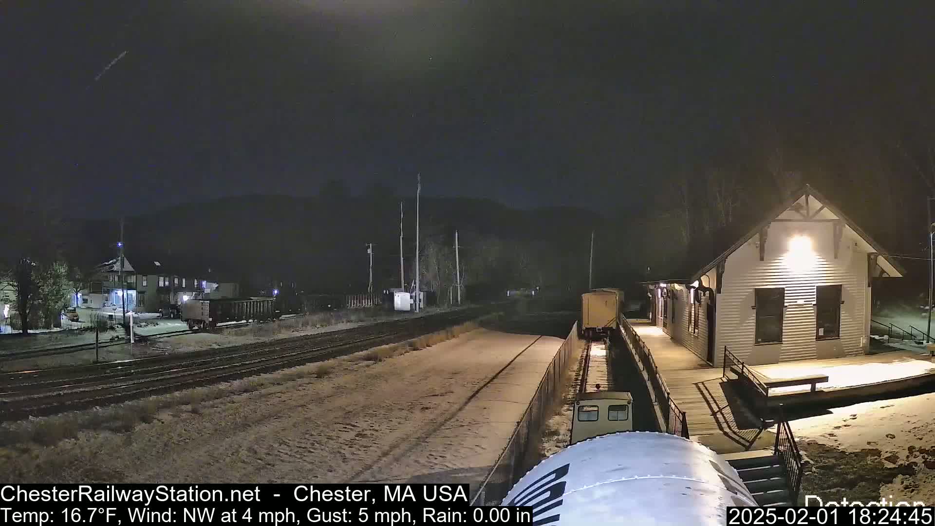 A train approaches a snow-covered train station at night under a dark sky.