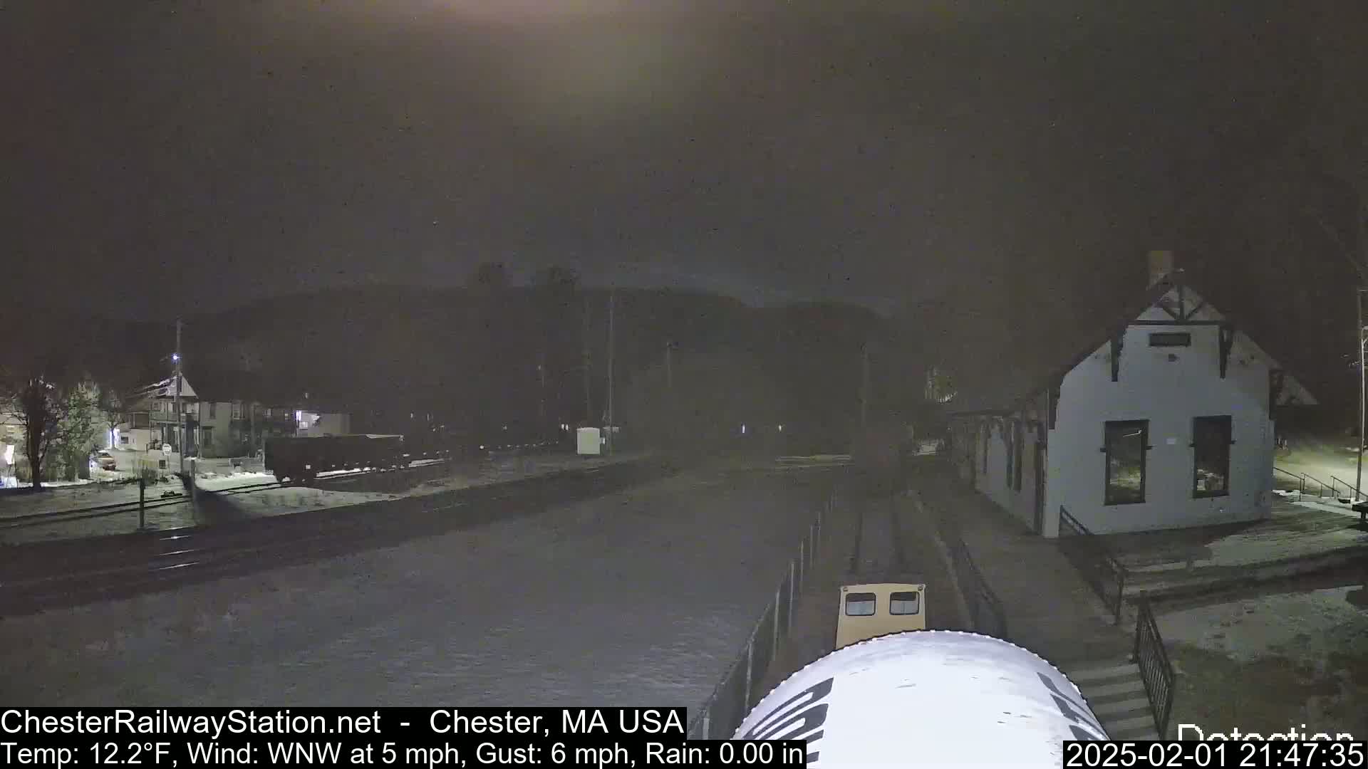 A nighttime scene of a train at a snow-covered station, under a dark sky with a temperature of 12.2°F and a WNW wind.