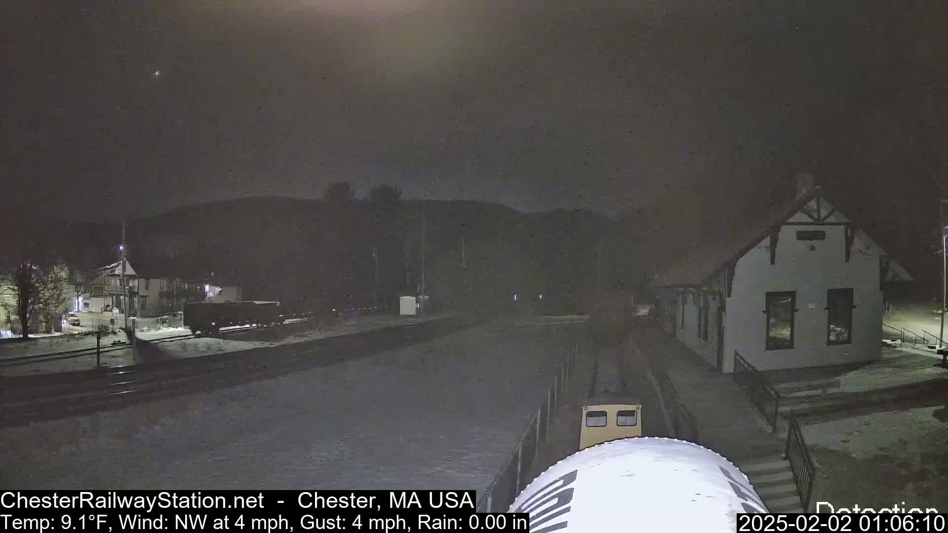 A nighttime view of a snow-covered train station and rail yard under a clear, dark sky.