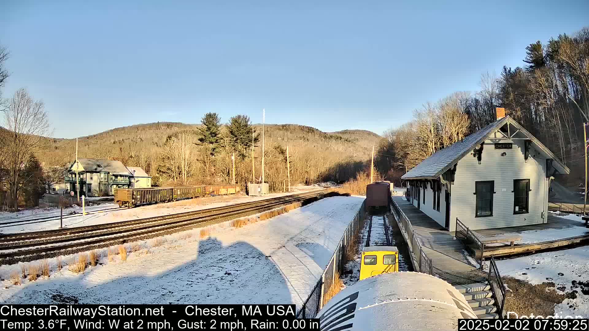A snow-covered train station and railway yard are nestled in a valley under a clear, sunny sky.