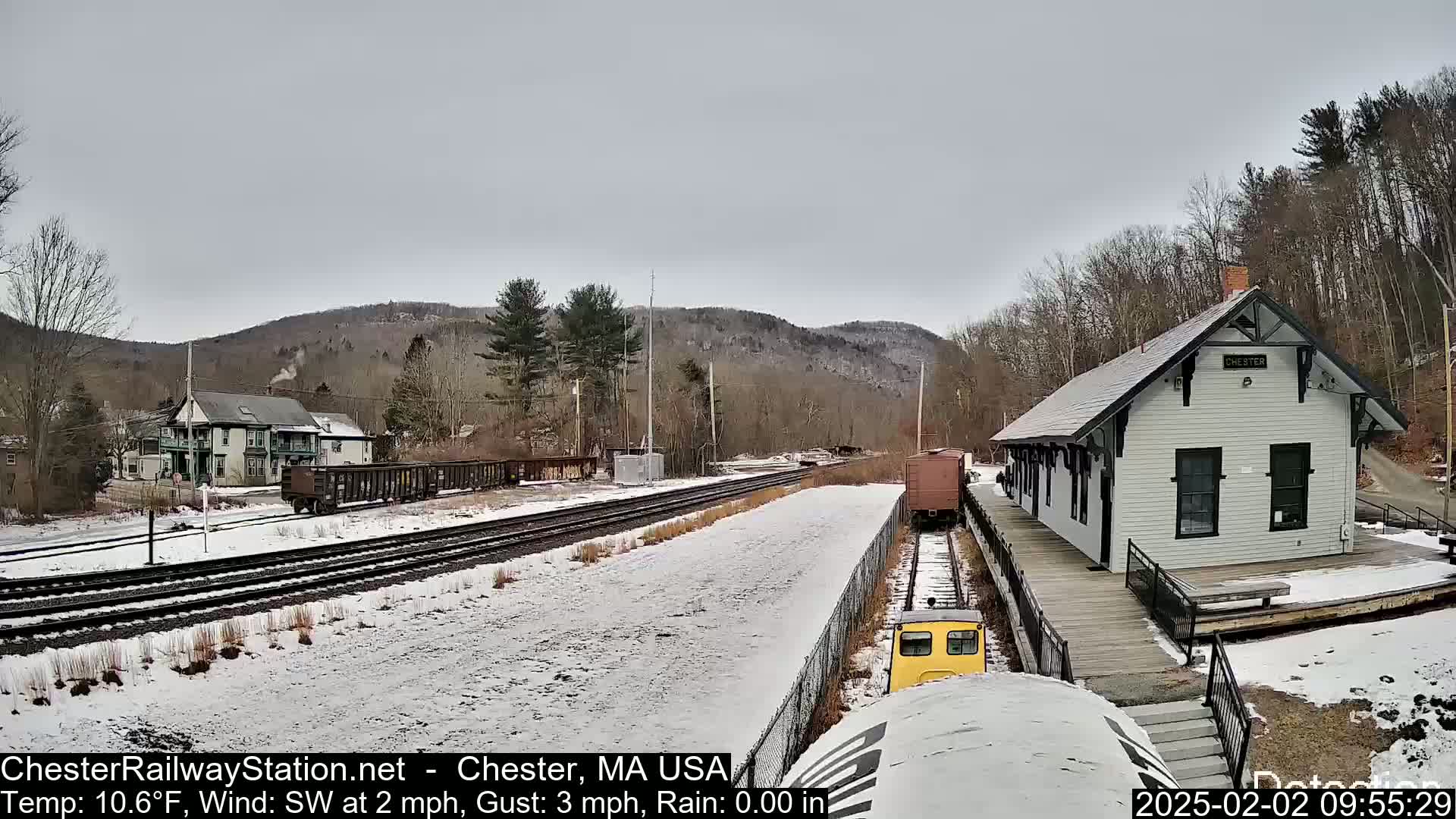 A snow-covered train station and tracks are visible, with a small train car nearby, under a gray sky.