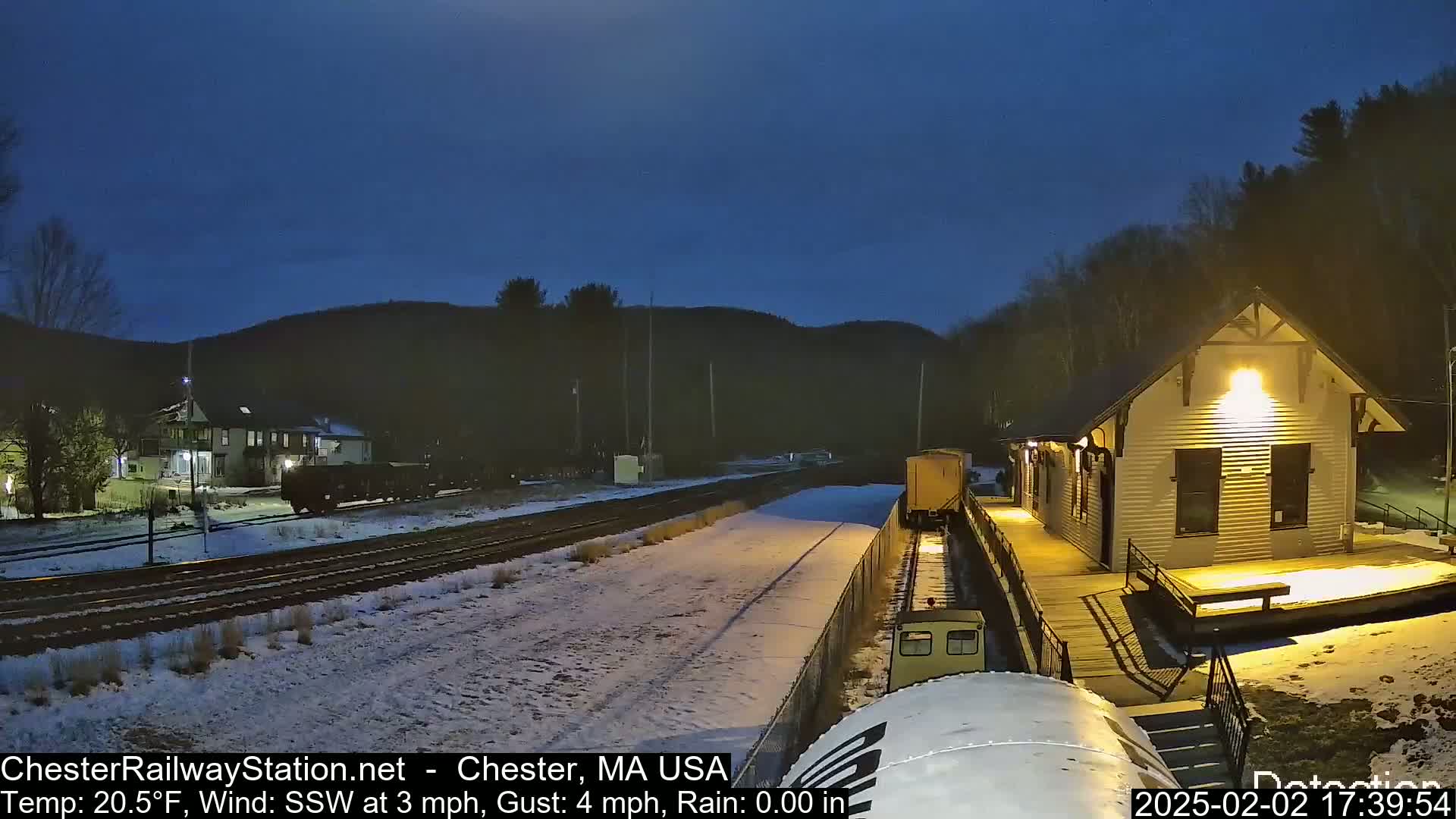A train passes a snow-covered train station at night under a dark blue sky.