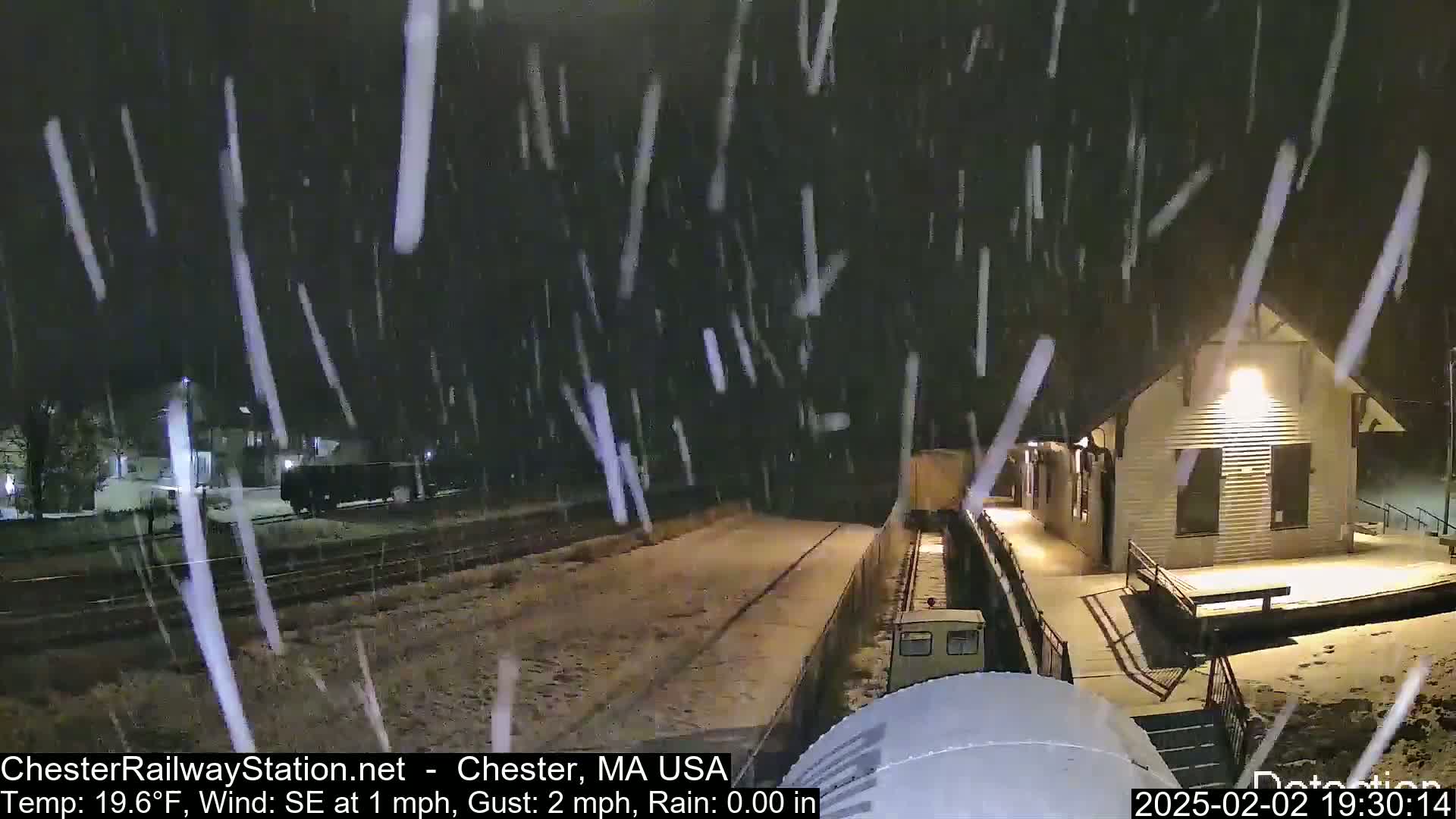 A train sits at a snow-covered train station during a nighttime snowfall.