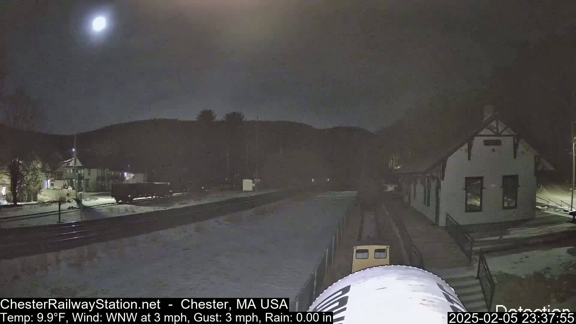 A train sits at a snow-covered station under a bright moon at night.