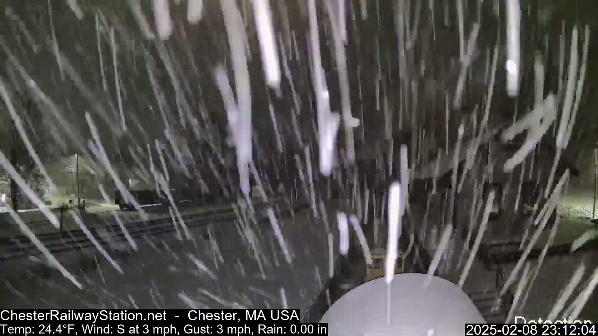 Heavy snowfall at night obscures a view of a street and buildings.