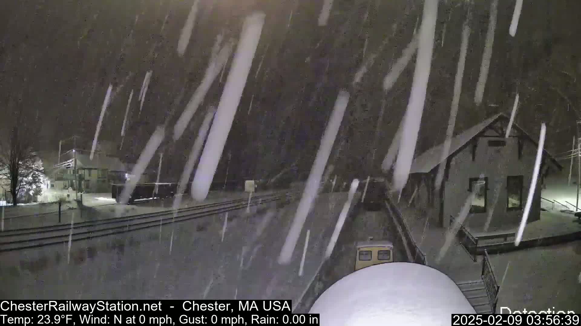 A snowstorm blankets a train station and surrounding area at night.