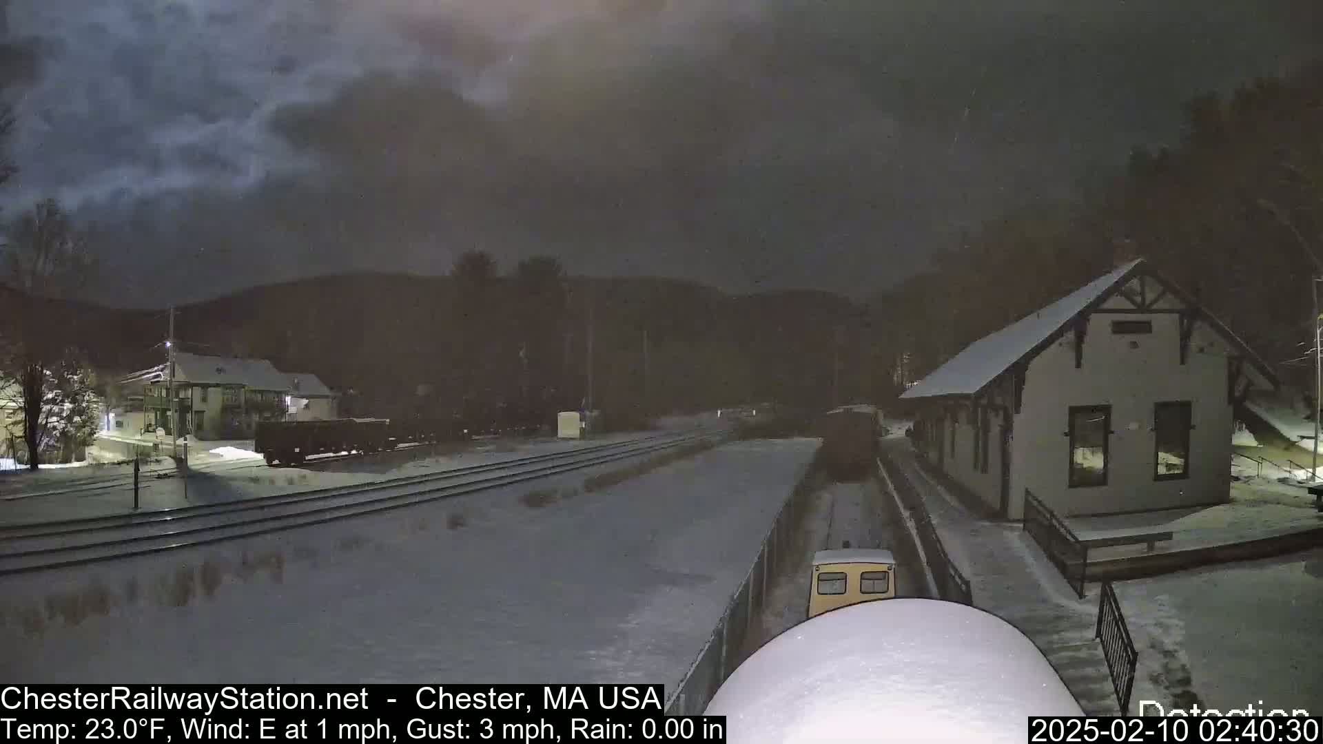 A snow-covered train station and railway tracks are visible under a dark, cloudy night sky.