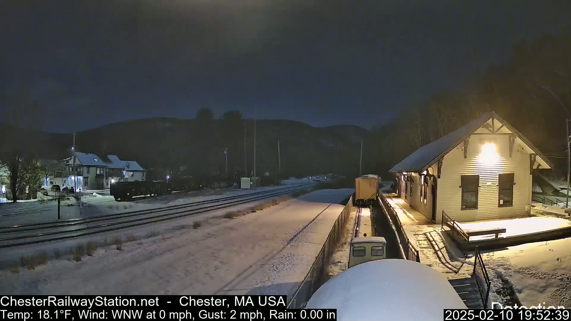 A snow-covered train station at night, with a train nearby, under a dark sky.