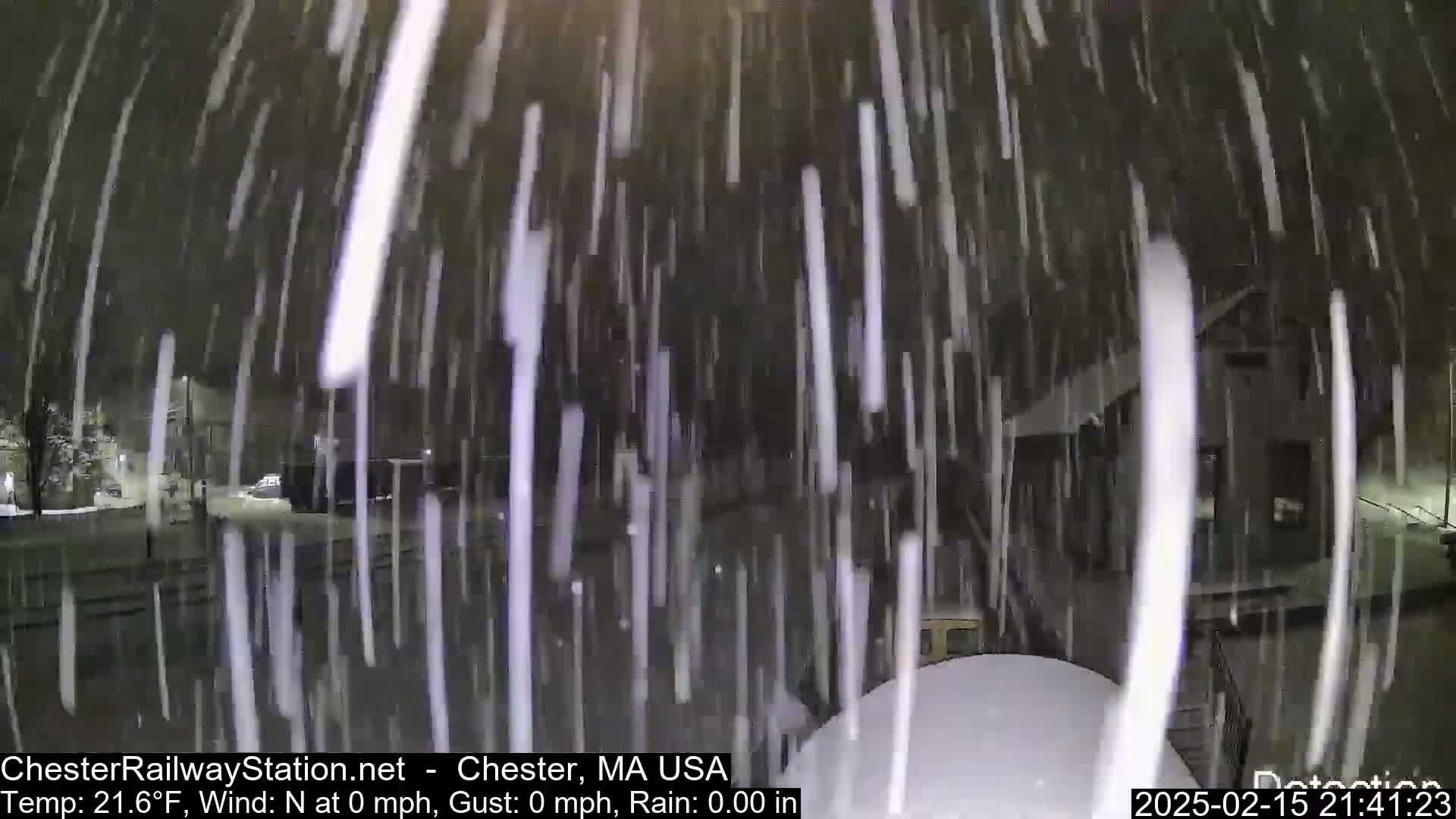 Heavy snowfall blankets a nighttime street scene, obscuring buildings and vehicles.