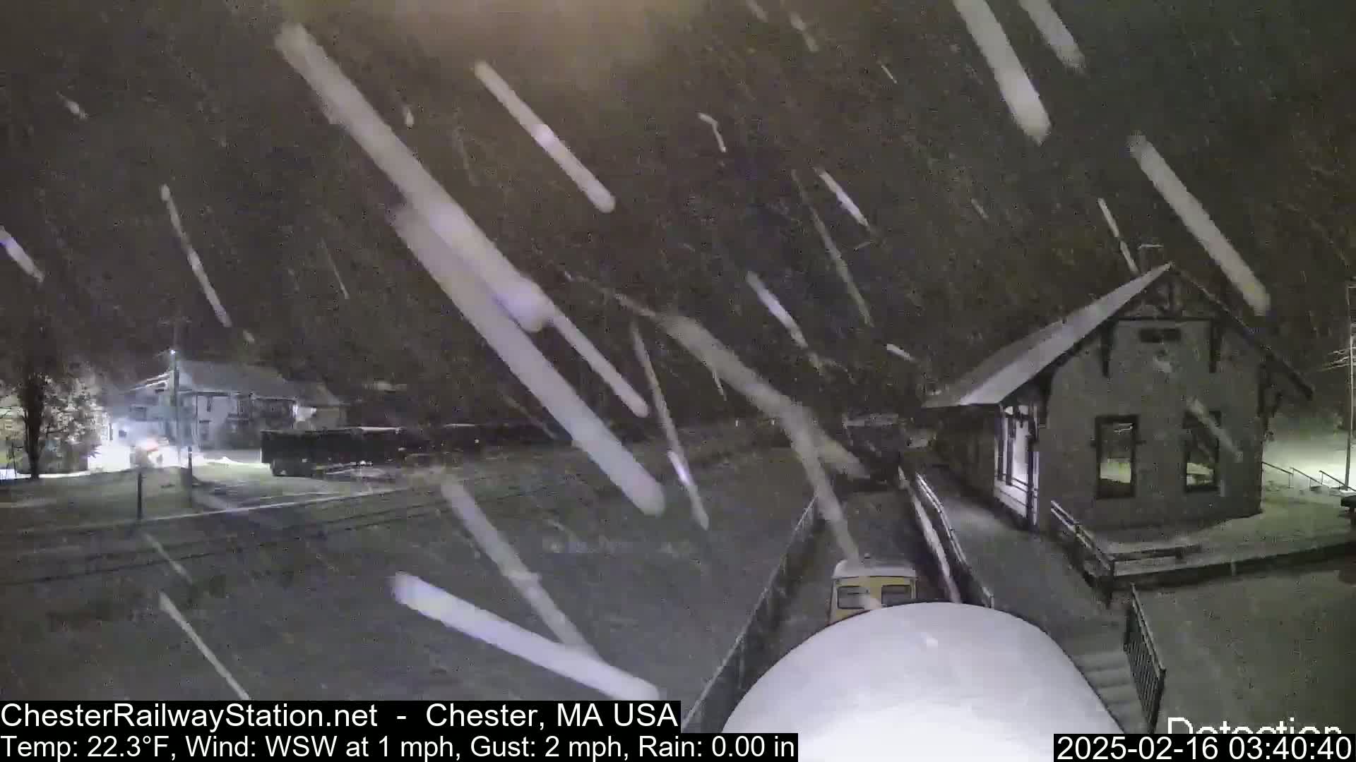 Heavy snow falls at night on a train station and surrounding area.