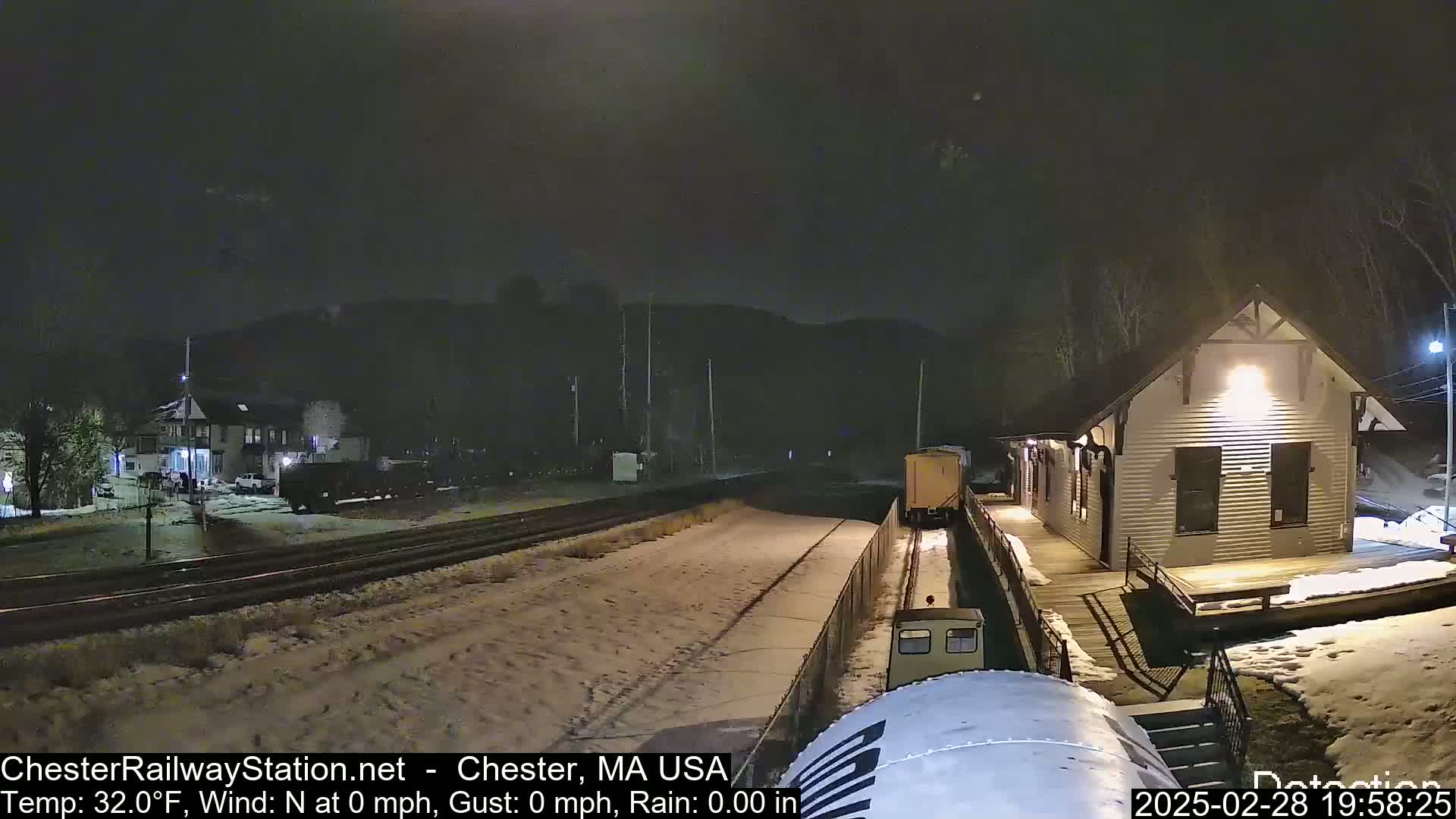 A snow-covered train station at night with a train car approaching, under a dark sky.