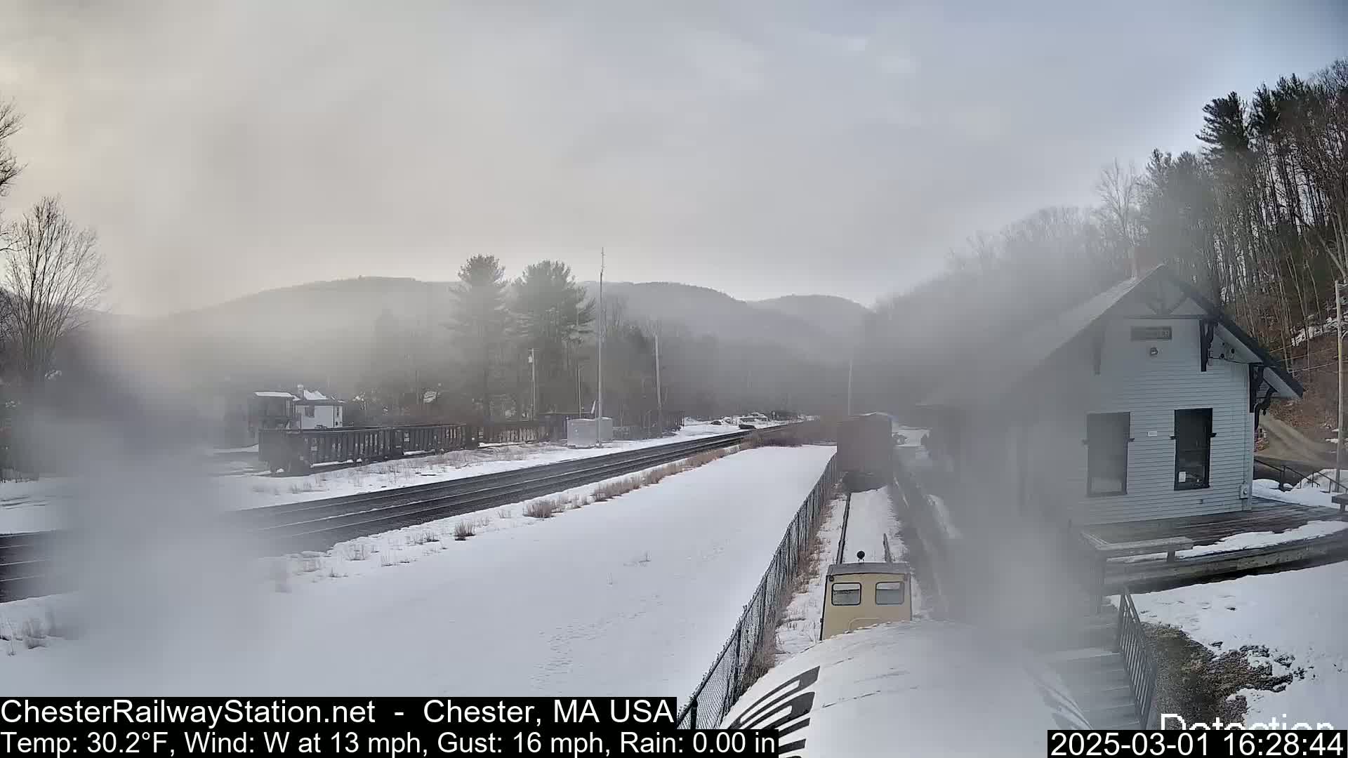 A snow-covered train station and tracks are visible in a foggy, cold landscape with a small train car in the foreground.