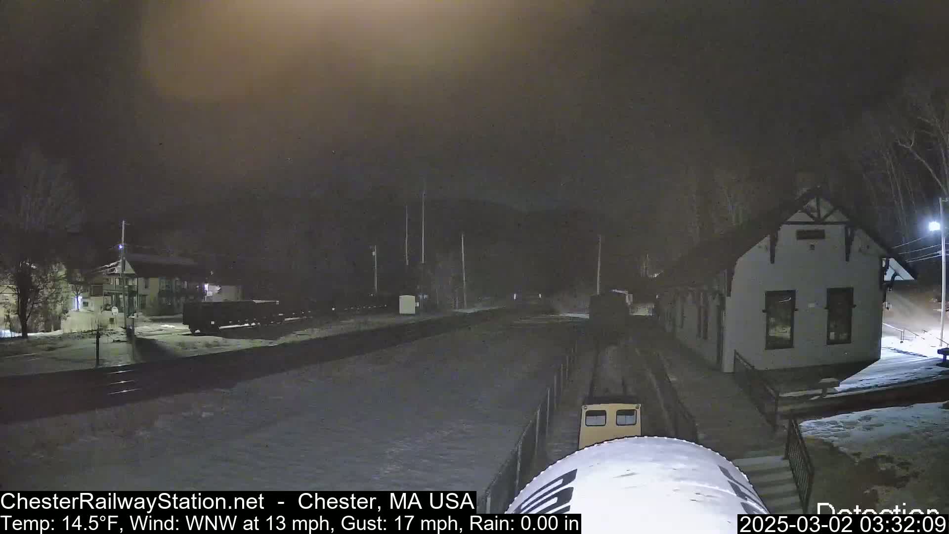 A snow-covered train station at night with a train partially visible, under windy conditions with a temperature of 14.5°F.