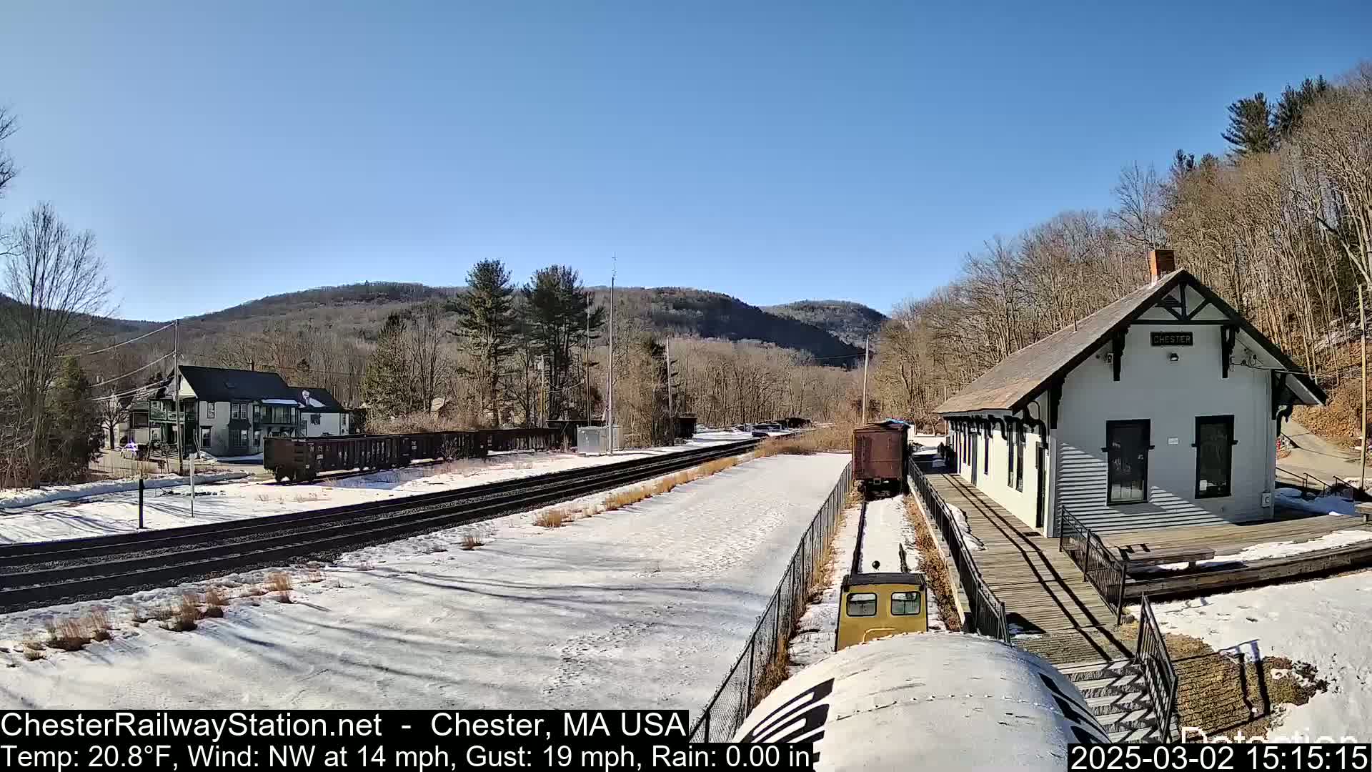 A snow-covered train station and railway yard are seen on a sunny day with a northwest wind.