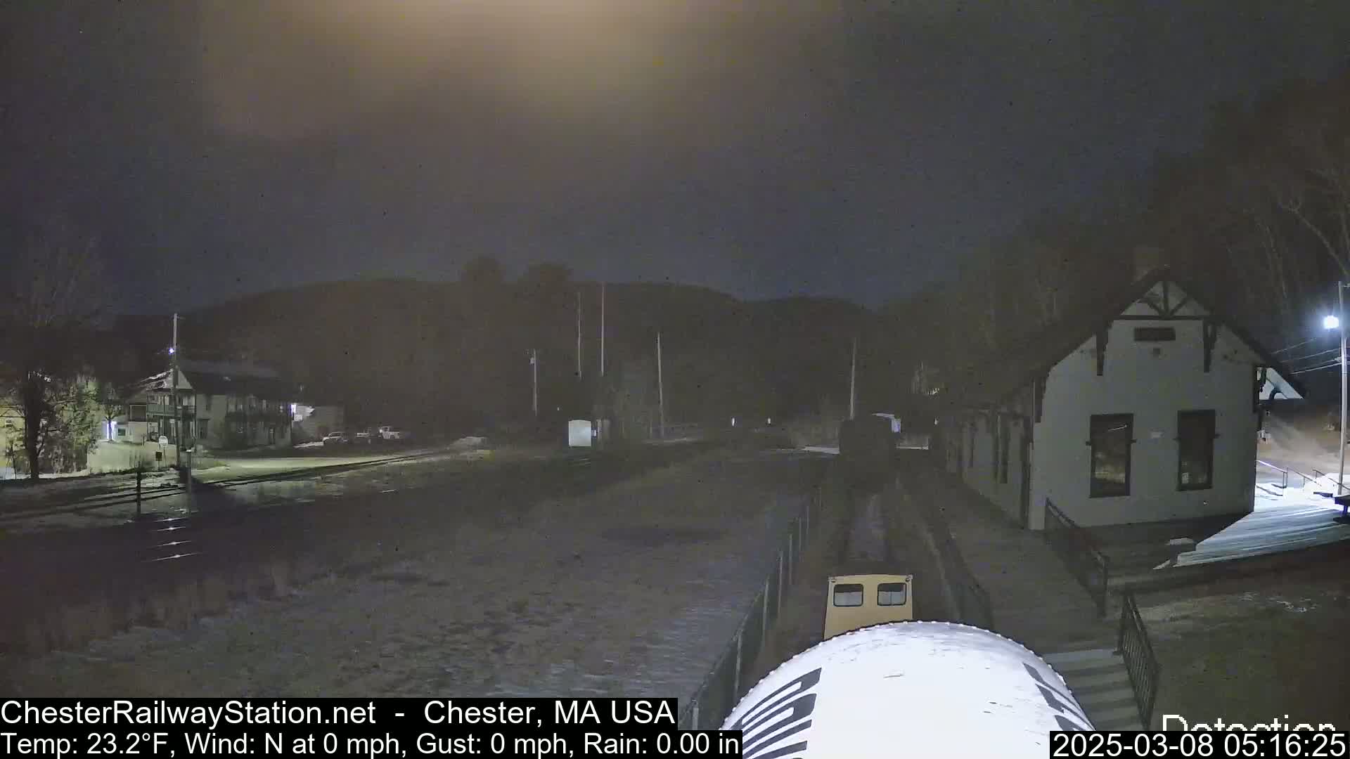 A nighttime view of a train station and surrounding area with a partly snowy ground under a dark sky.