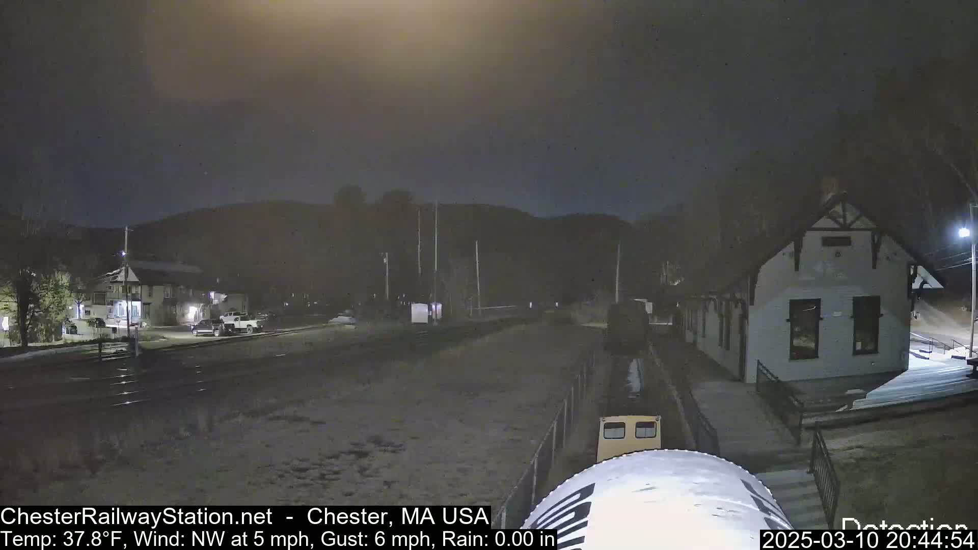 A nighttime scene shows a train at a station, with light snow on the ground and a northwest wind.