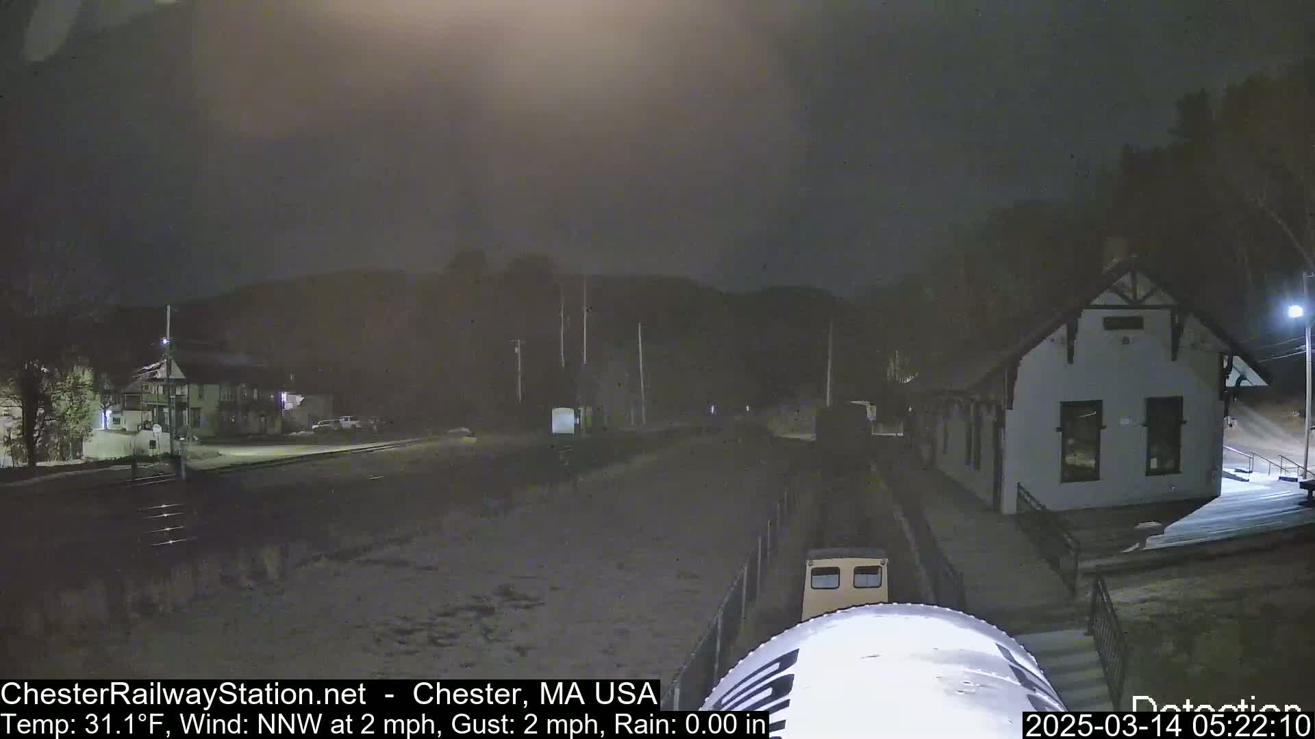 A nighttime view of a train at a snow-covered station under rainy conditions.