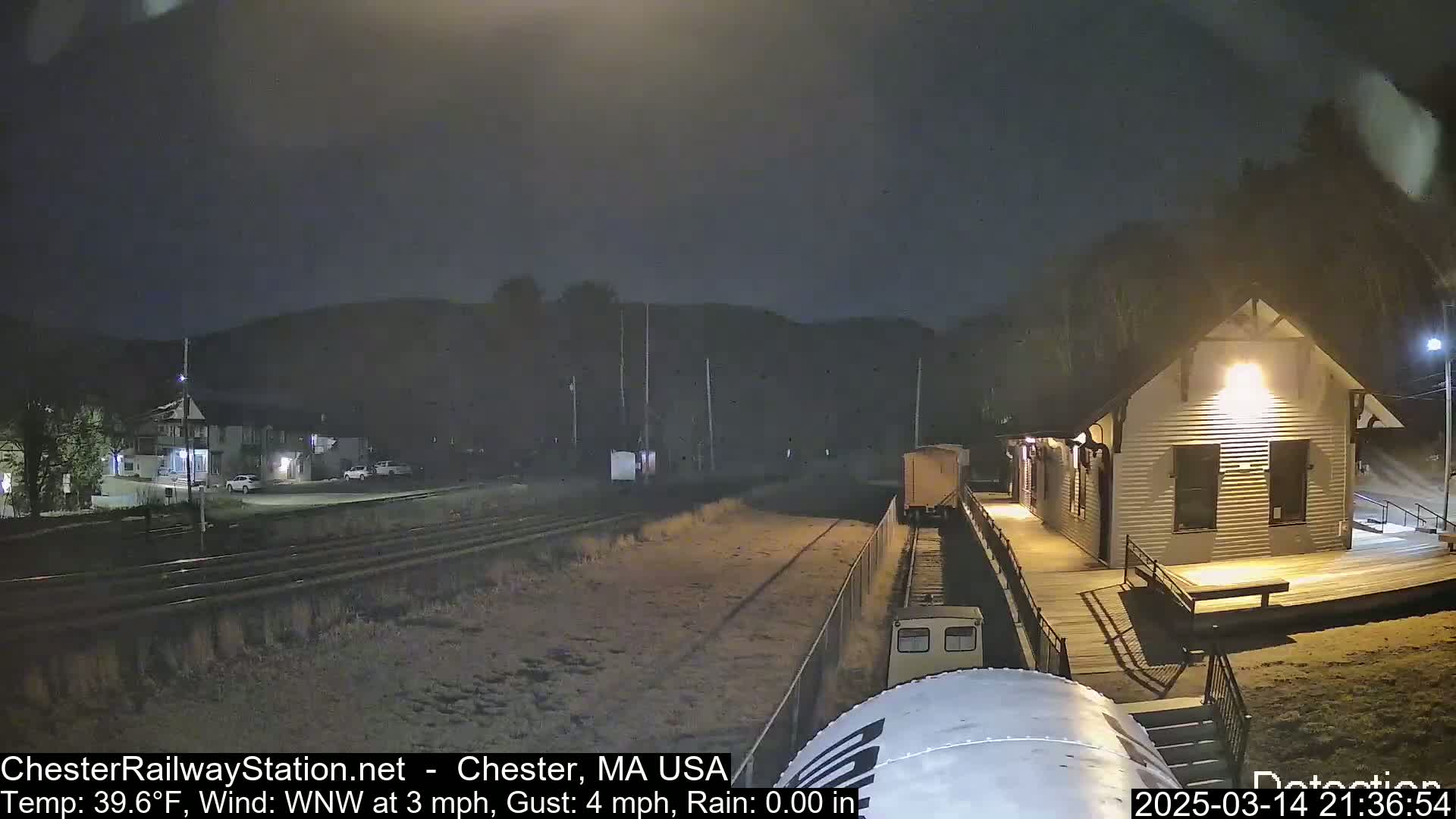 A nighttime view of a train arriving at a small, illuminated station under rainy conditions.