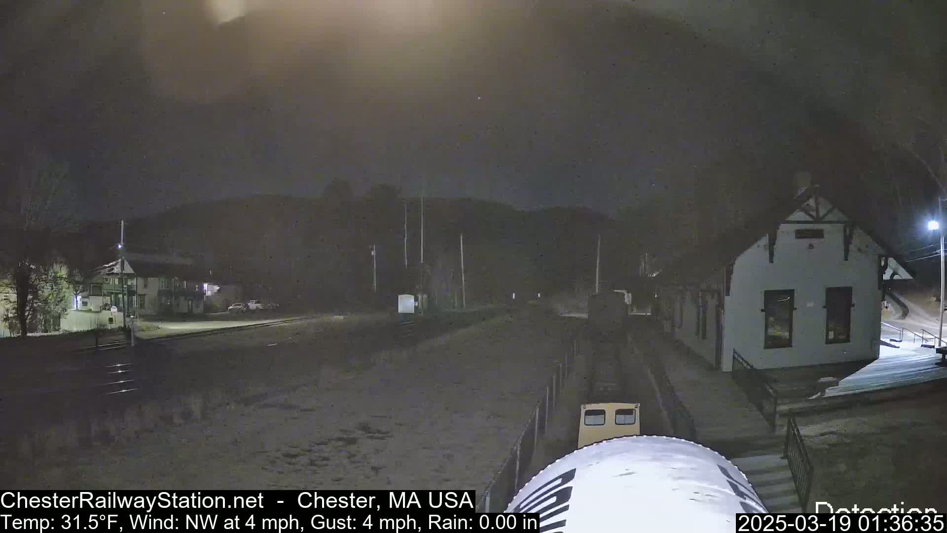 A nighttime view of a train approaching a snow-covered train station under a dark, overcast sky.