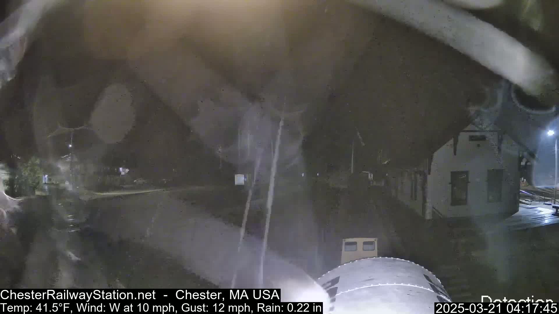 A nighttime view of a wet street and a building under rainy conditions with a wind from the west.