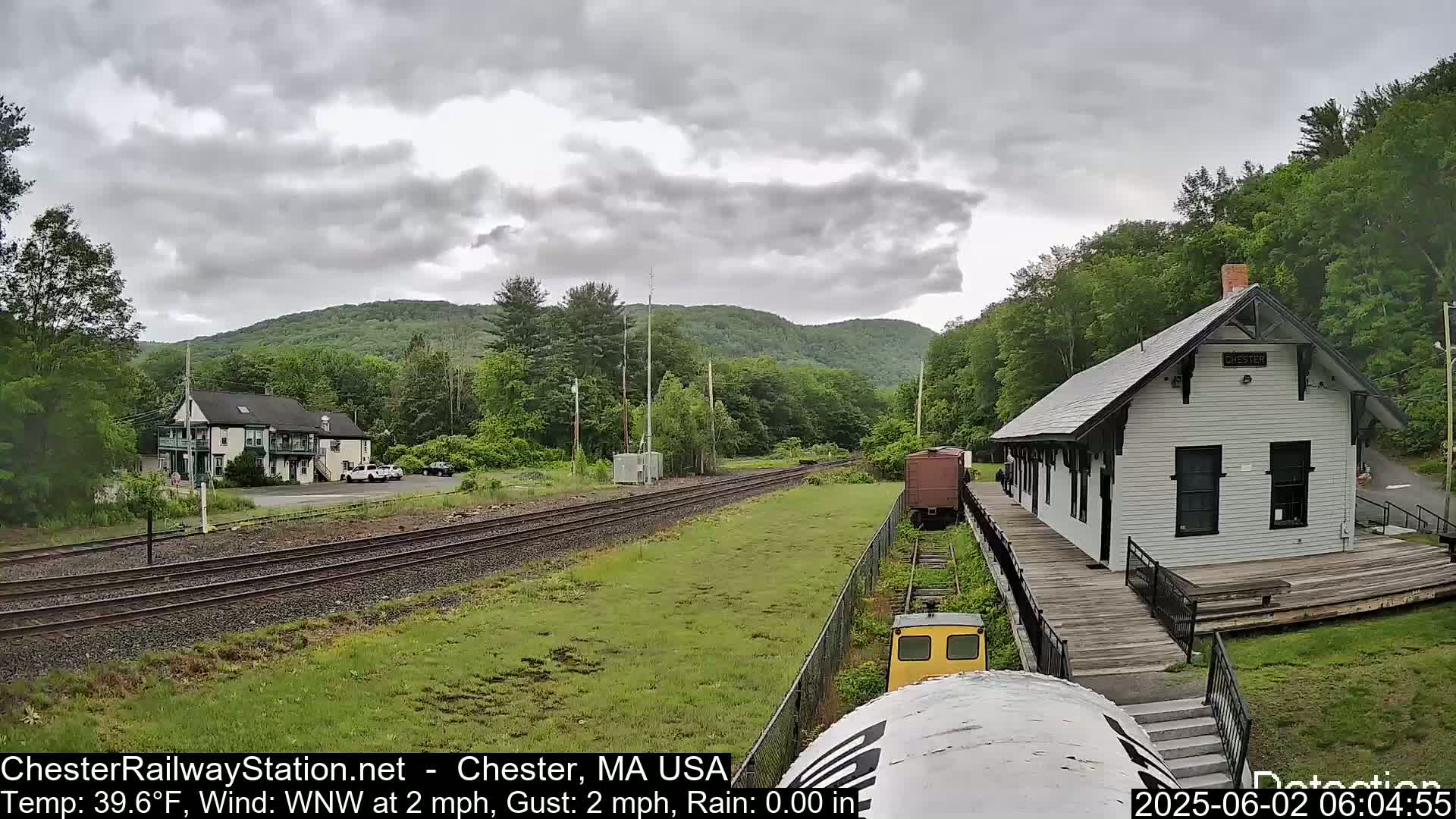 A train station and rail yard are visible under a cloudy sky, with a small train car parked on a side track.