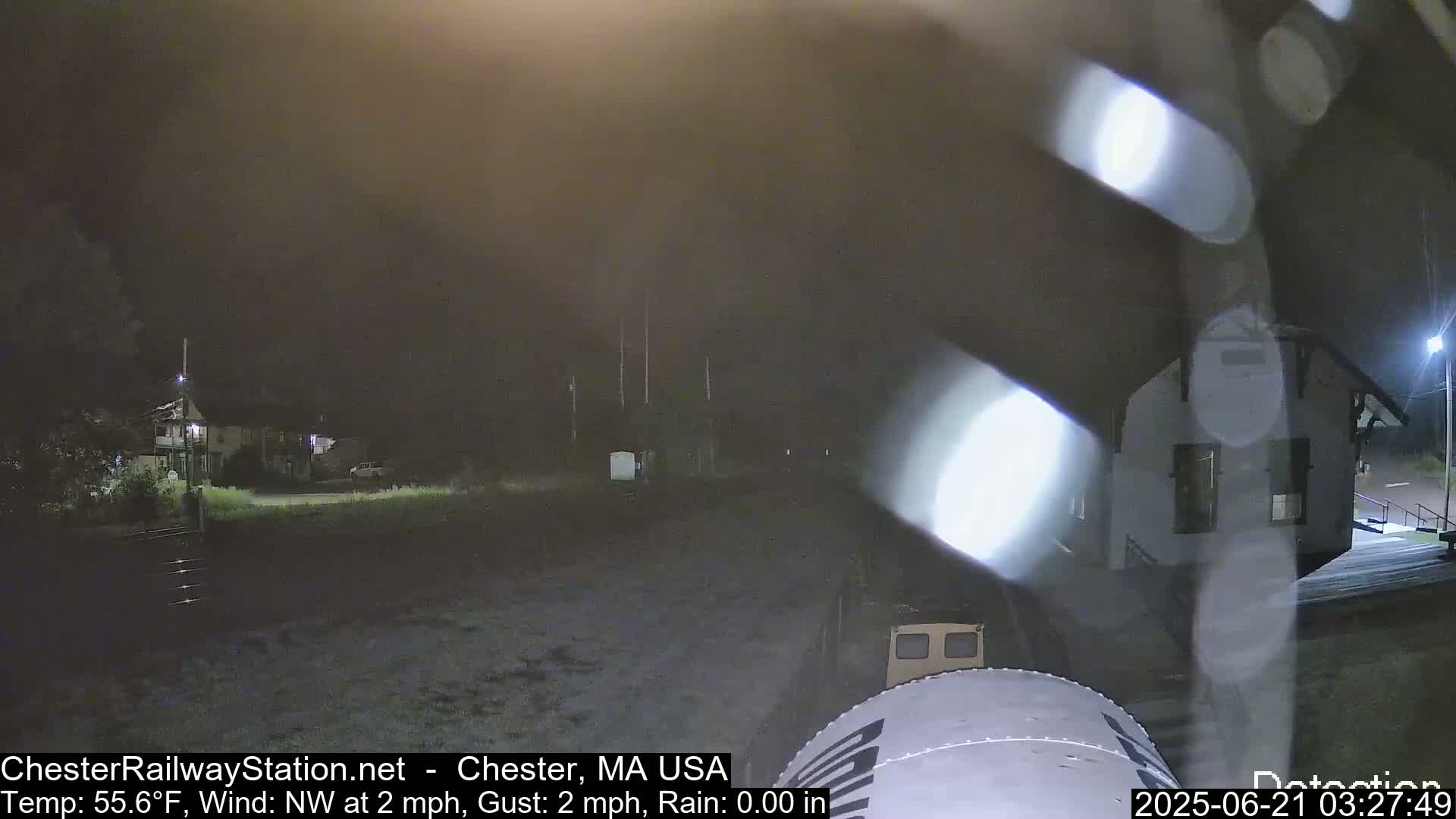A nighttime view of a train car in front of a building, under slightly hazy conditions with a light northwest wind.