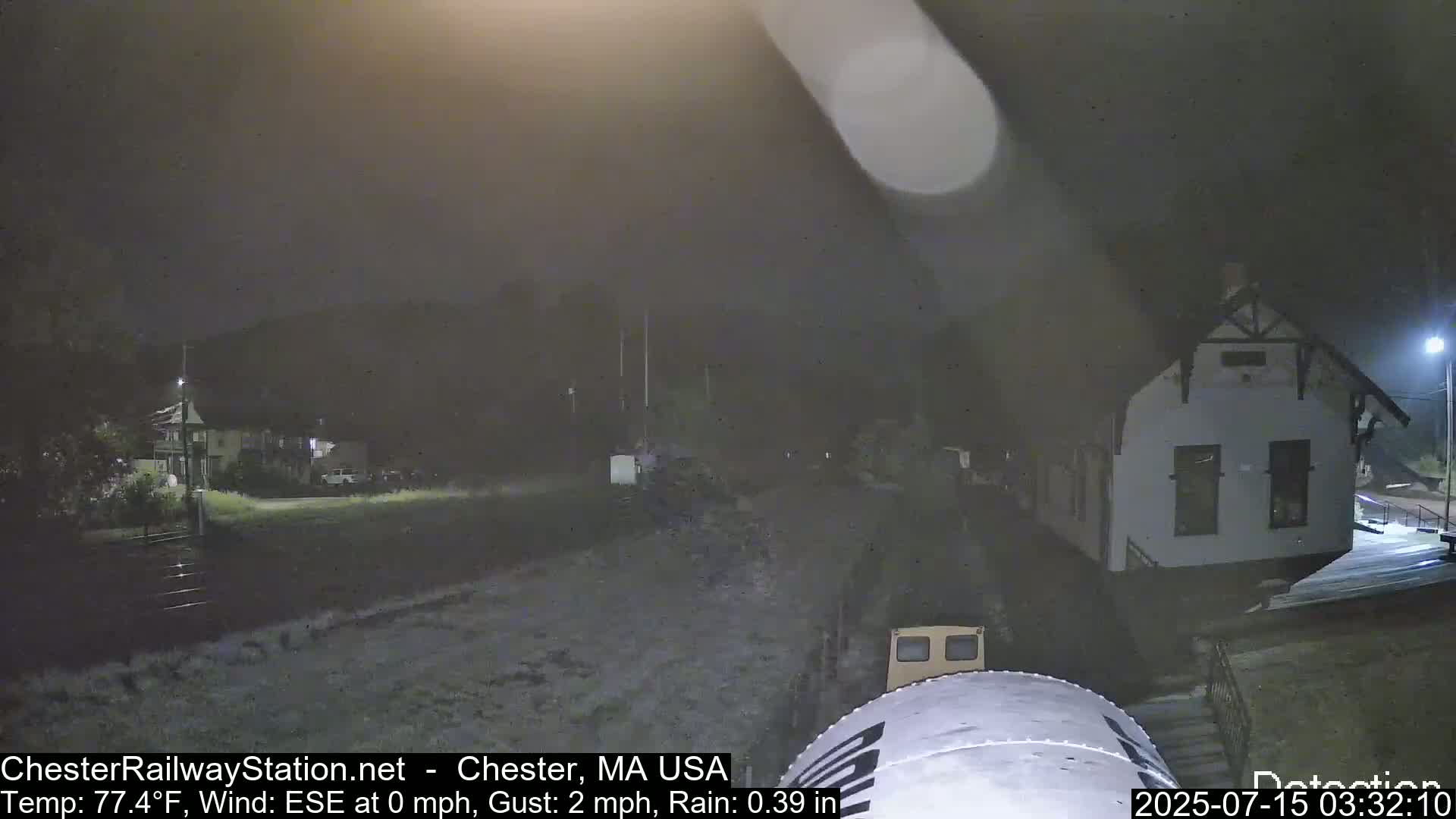 A nighttime scene shows a small building, lightly raining, with a vehicle partially visible in the foreground.
