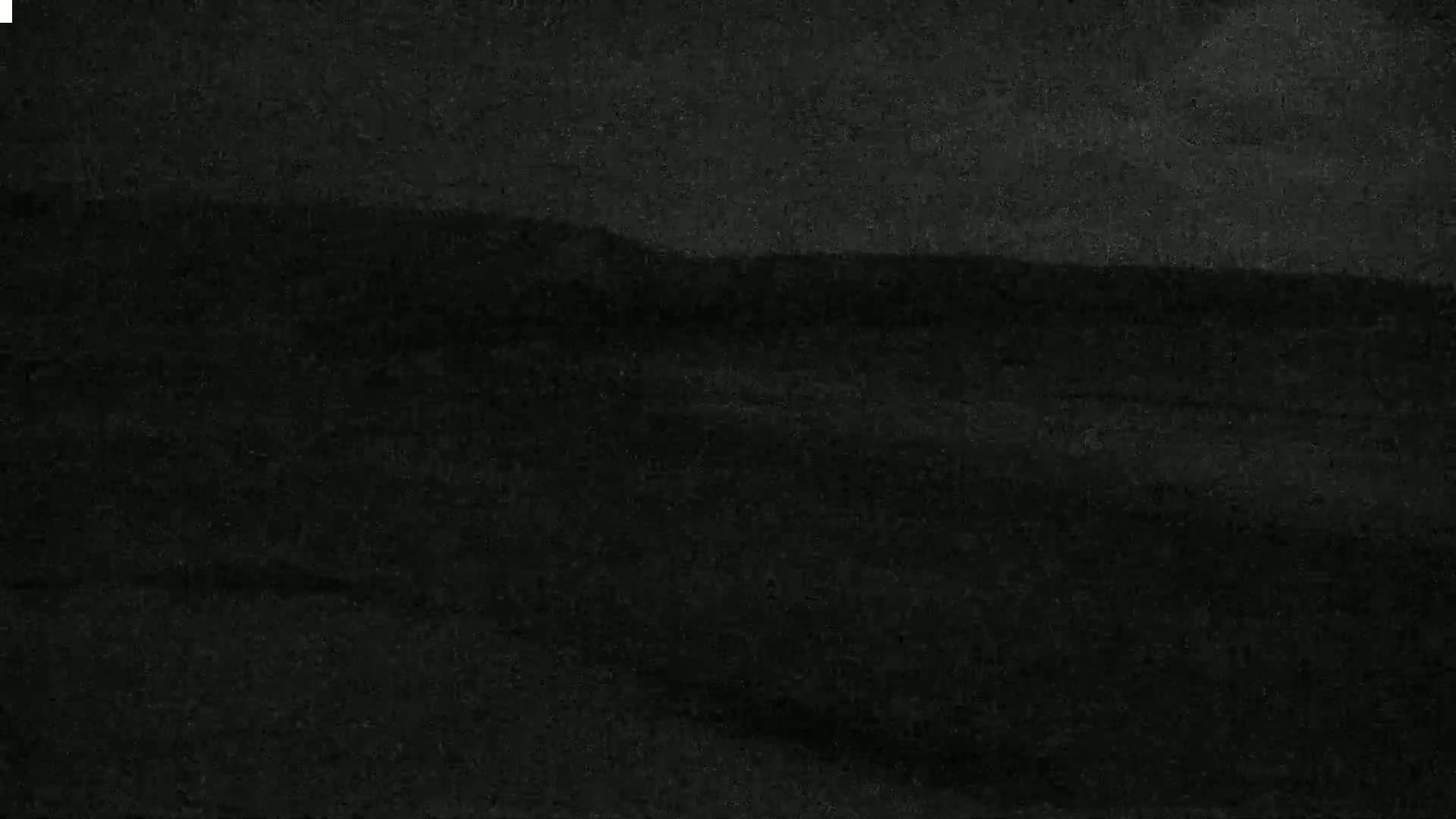 A dark, possibly nighttime, image shows a blurry landscape of low hills or rolling terrain.