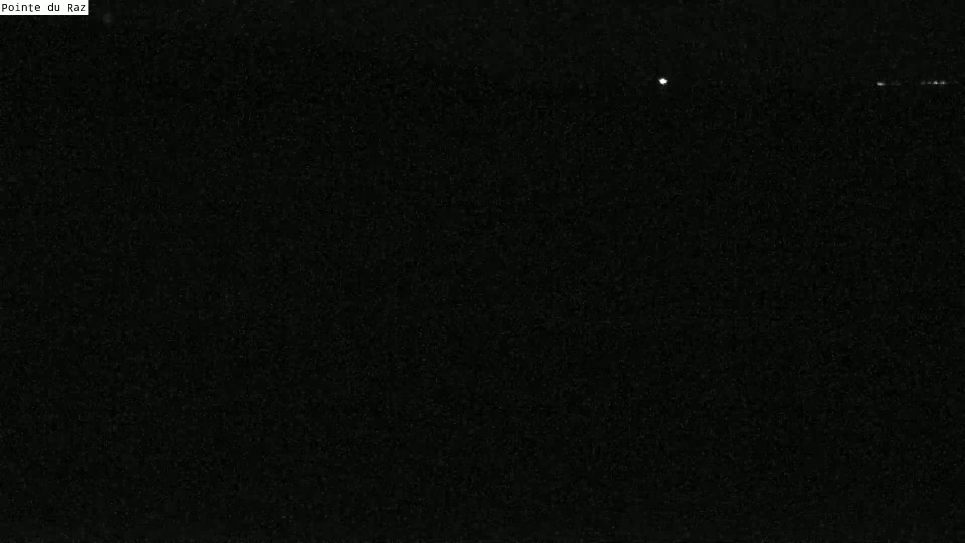 A nearly completely dark image shows a few faint lights in the distance at night.
