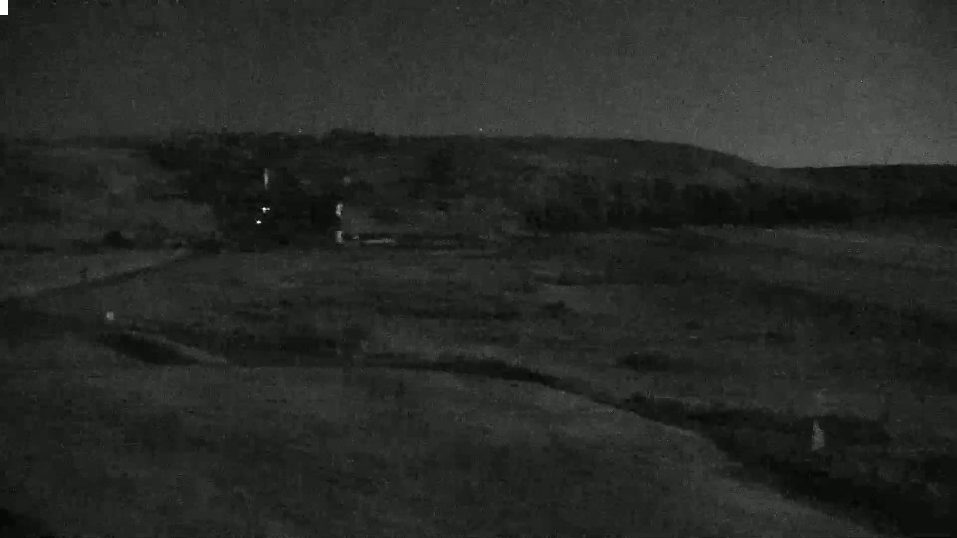 A dark, nighttime view of a hilly landscape with sparse vegetation under a clear sky.