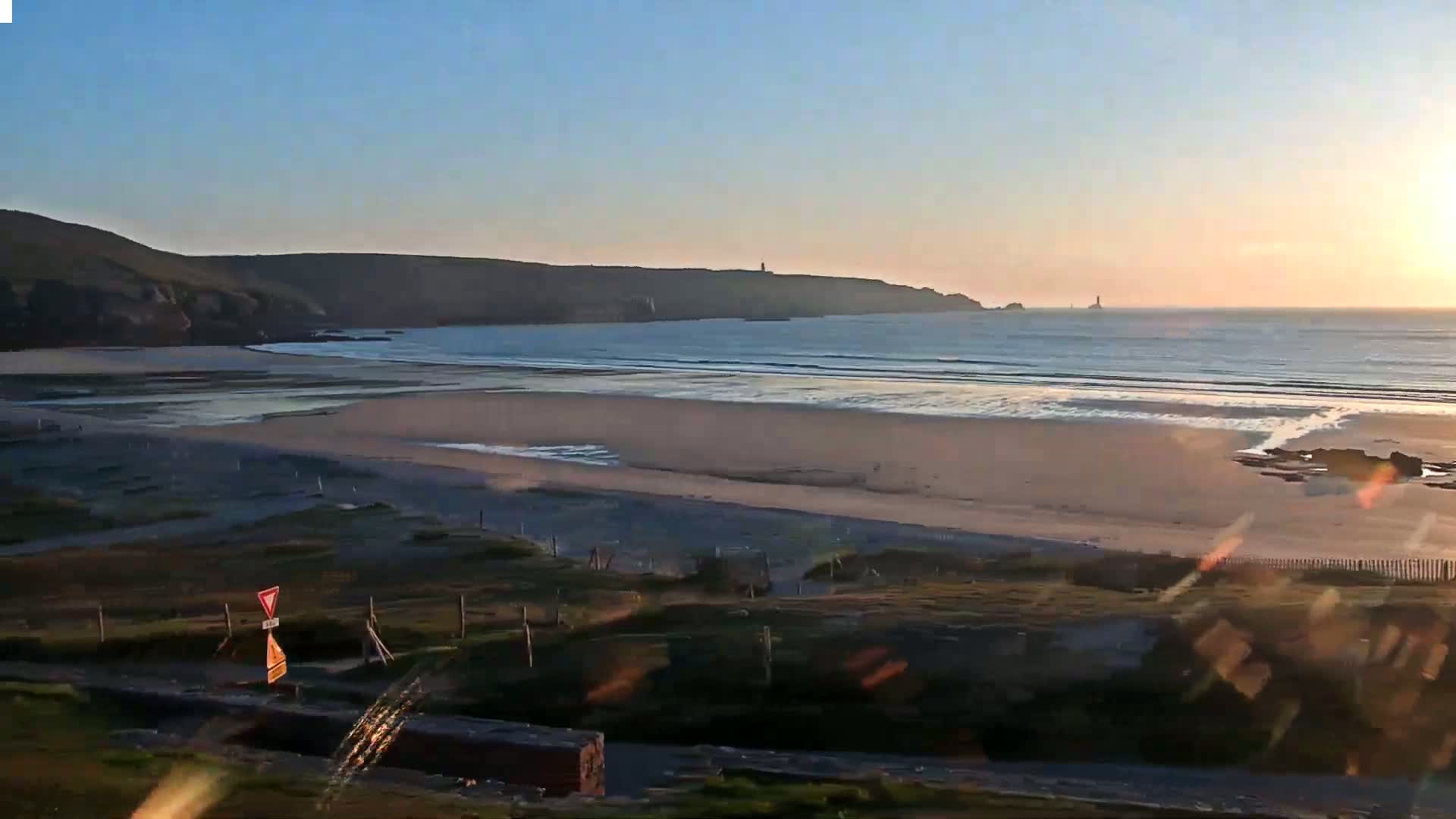A wide sandy beach stretches along a calm ocean under a clear sunset sky.