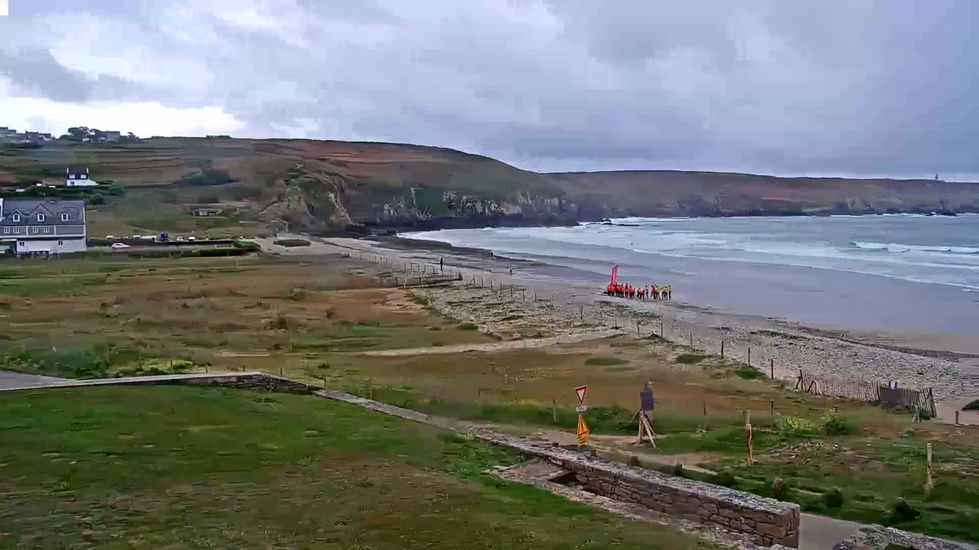 A group of people stands on a beach with gray, overcast skies and moderate waves rolling onto the shore.