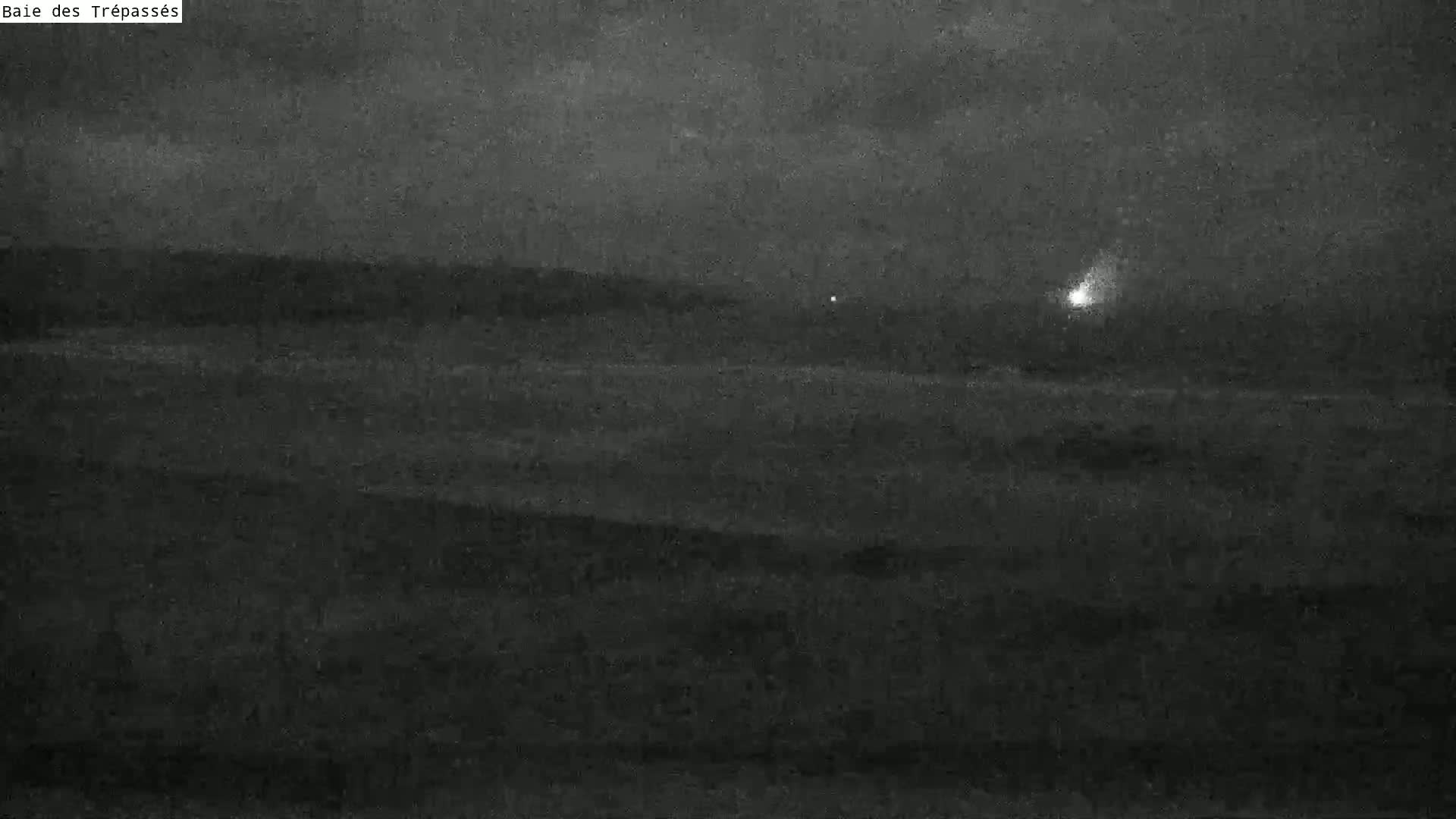A dark, nighttime landscape shows a body of water under an overcast sky, with a single, distant light visible on the horizon.