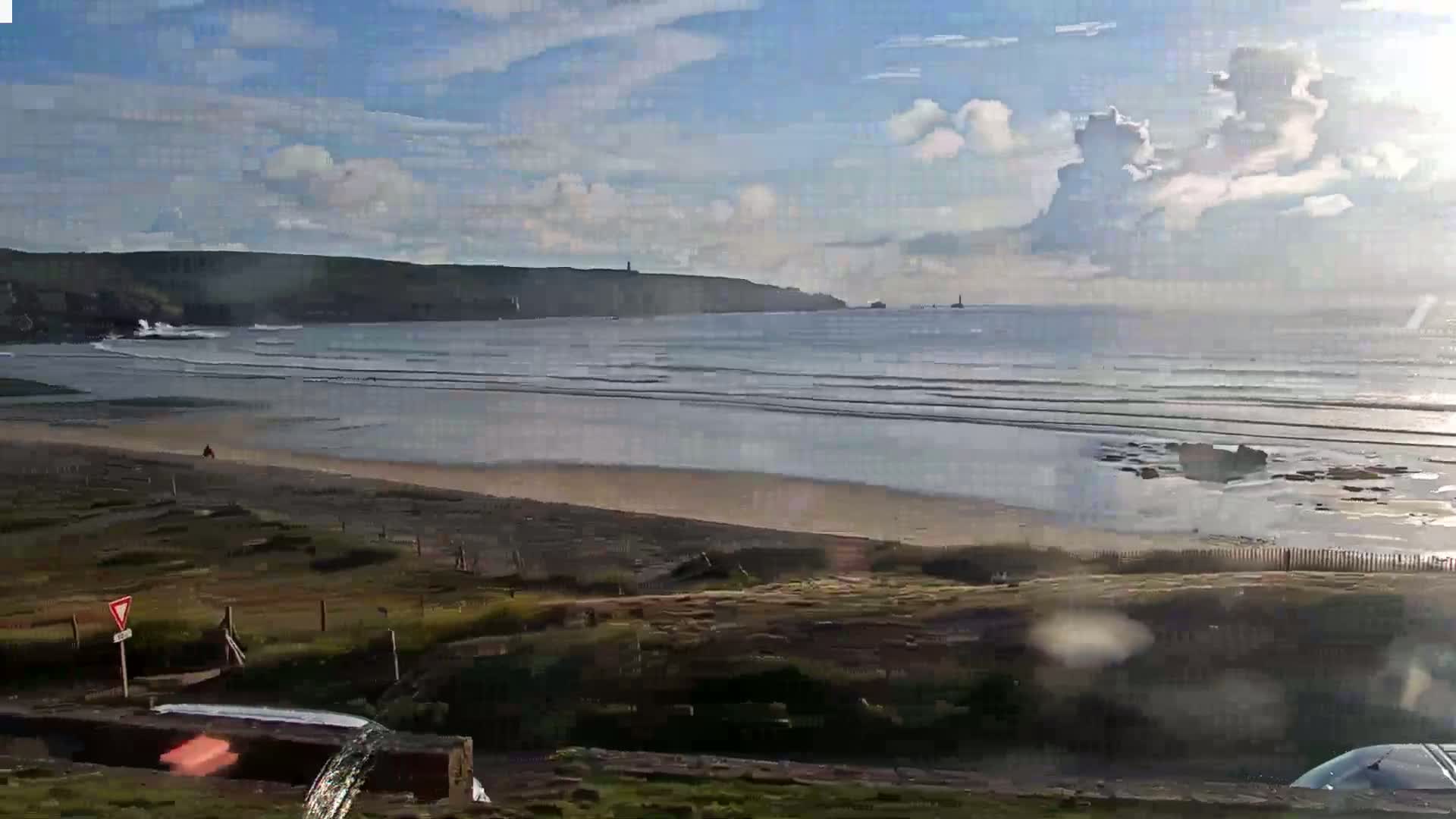A sandy beach stretches out to a calm sea under a partly cloudy sky, with distant headlands visible.