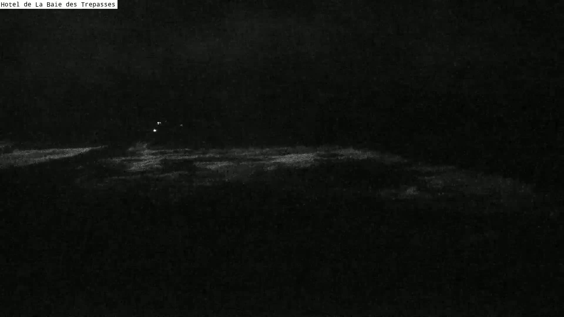 A dark, nighttime scene shows a dimly lit horizon line, possibly of water, under a dark sky.