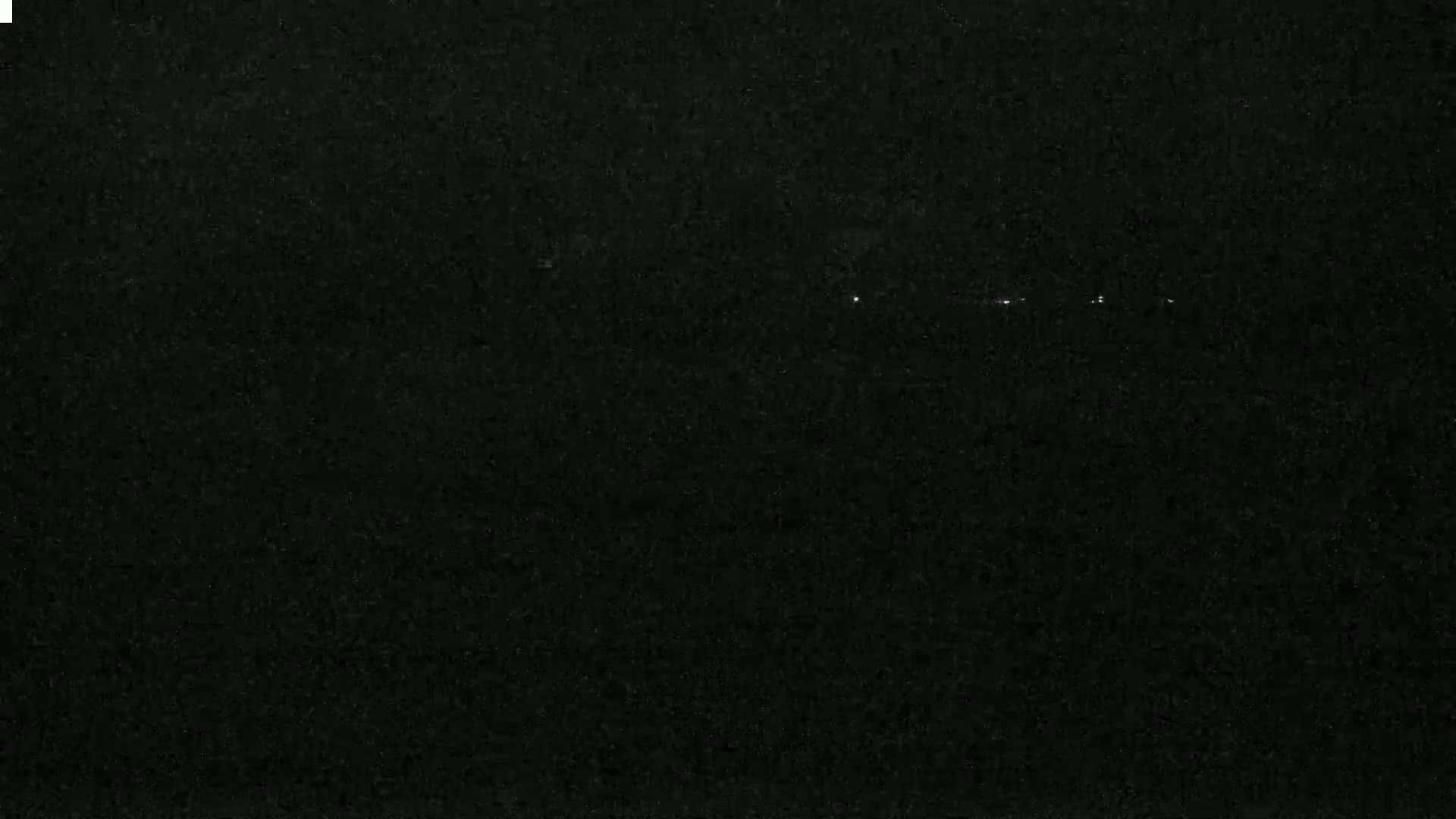 A dark, nighttime scene shows a few faint lights in the distance.