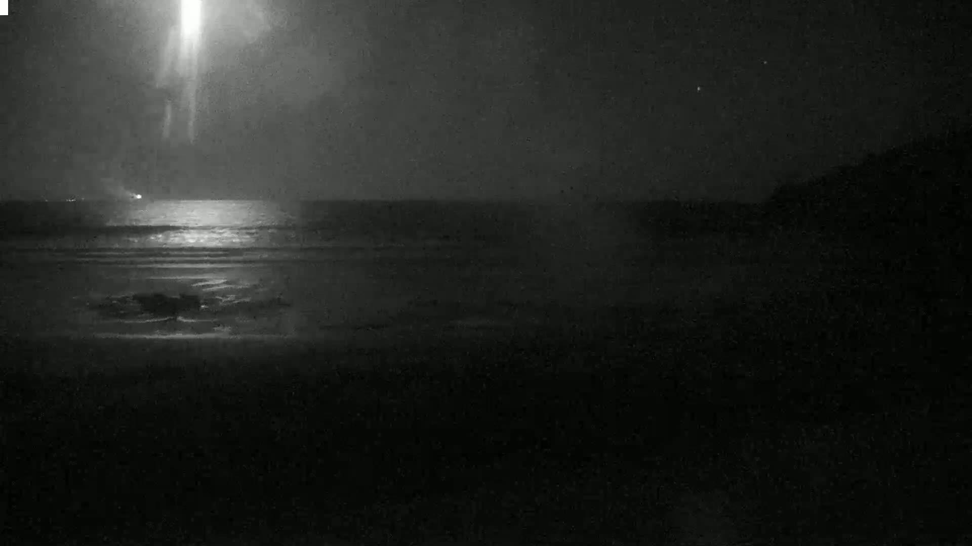 A bright light shines over a dark ocean at night.