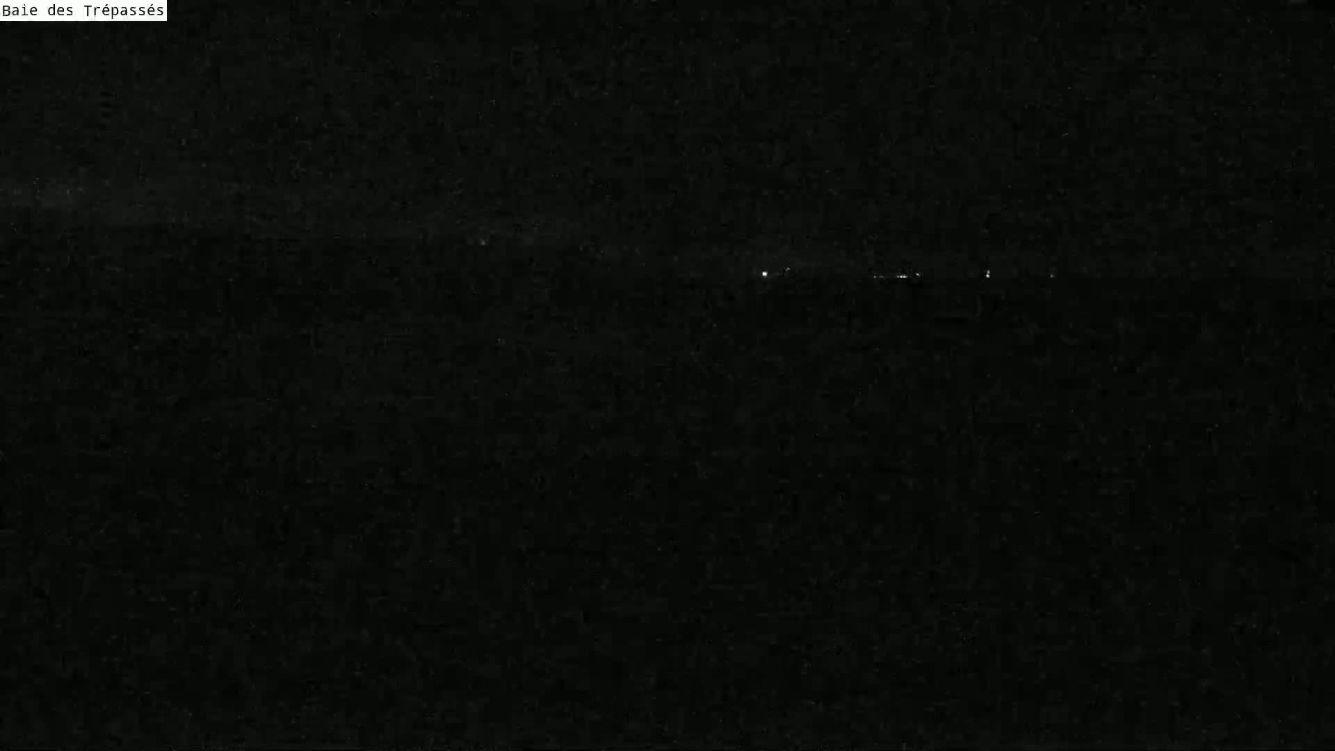 A dark, nighttime scene shows a faint line of distant lights on the horizon.