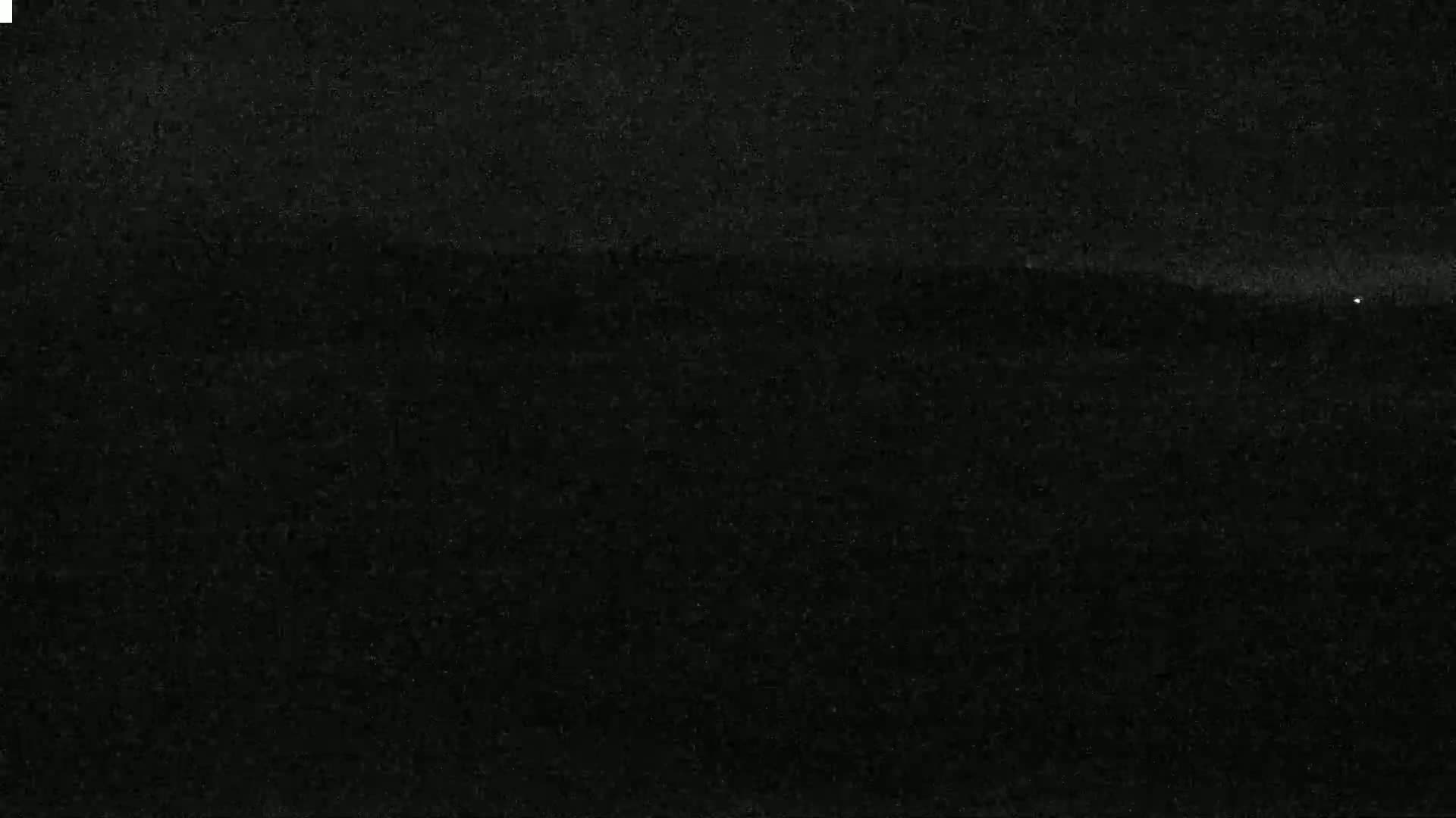 A dark, possibly nighttime, image shows a faintly visible horizon line with a few specks of light.