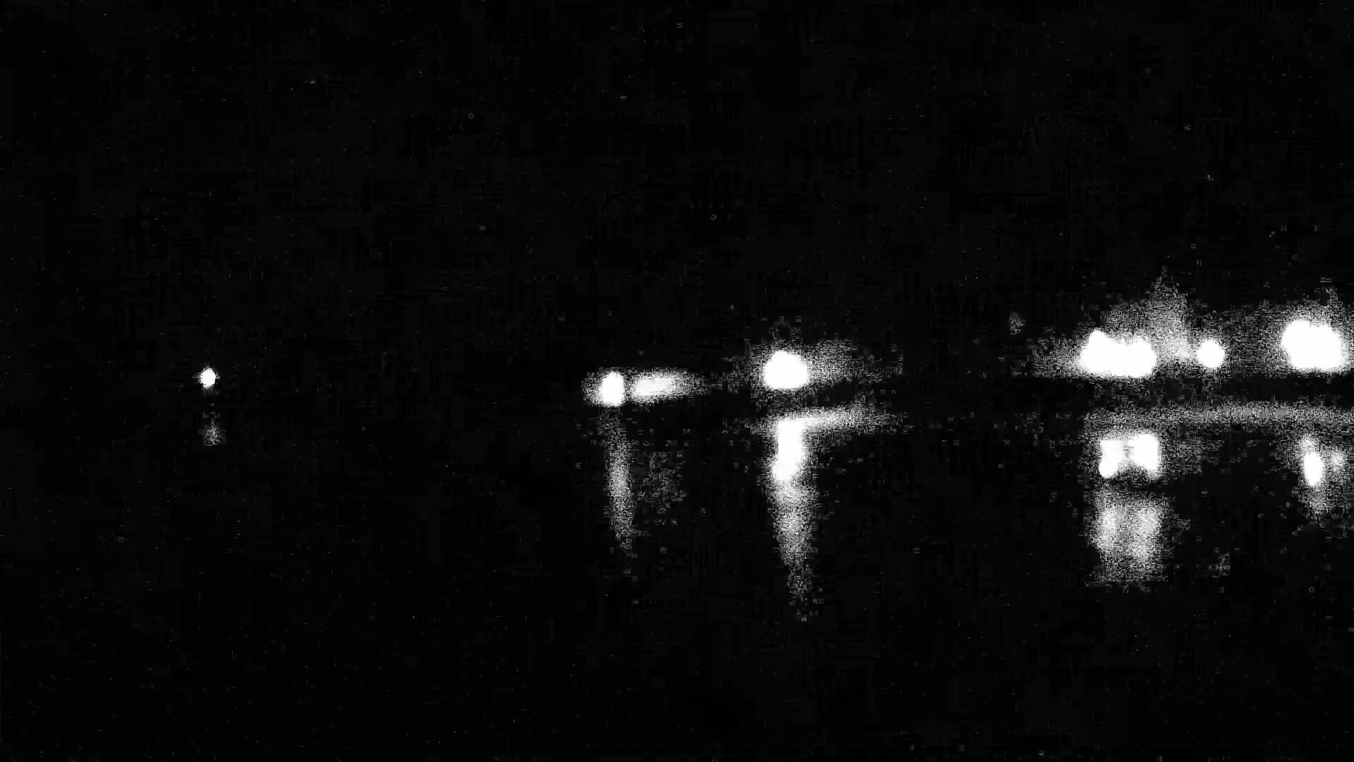 A nighttime view shows blurry lights reflecting on water, with a single, distant light source visible to the left.