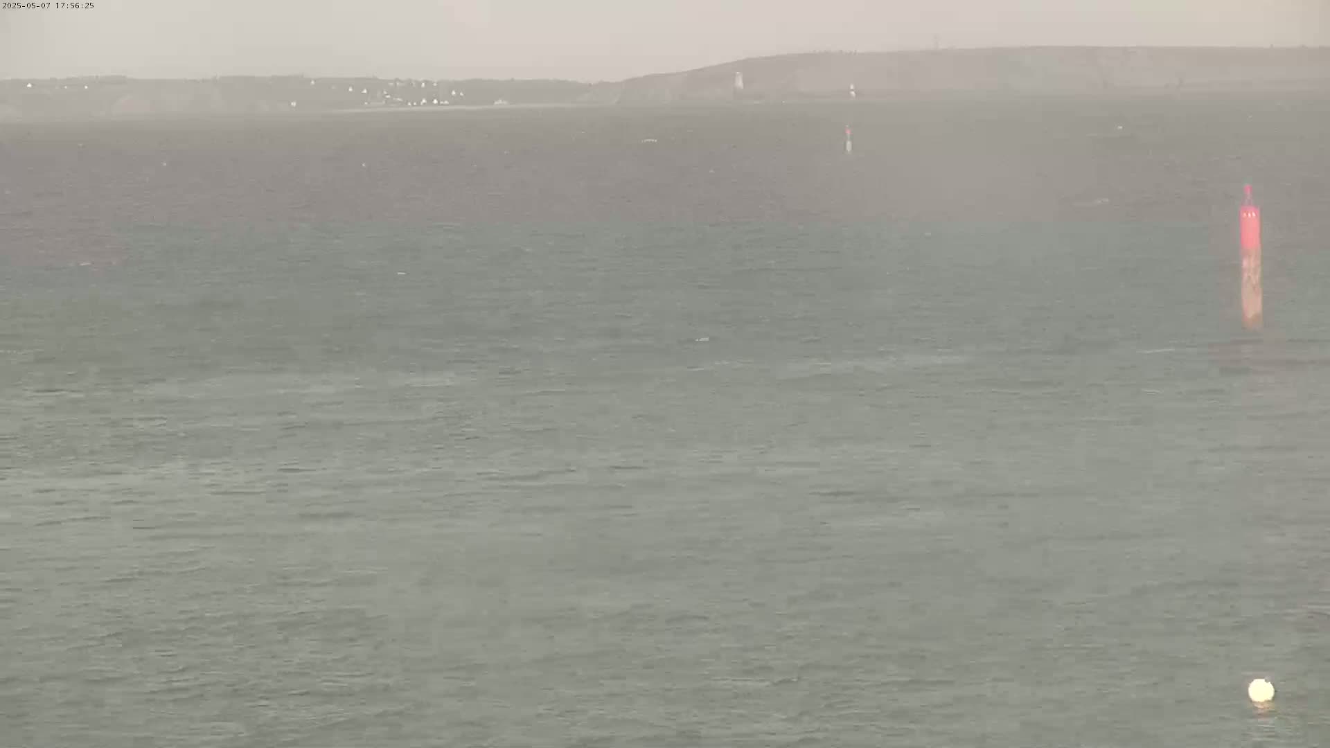 A hazy, overcast day shows a choppy sea with a distant shoreline and a few navigation buoys.