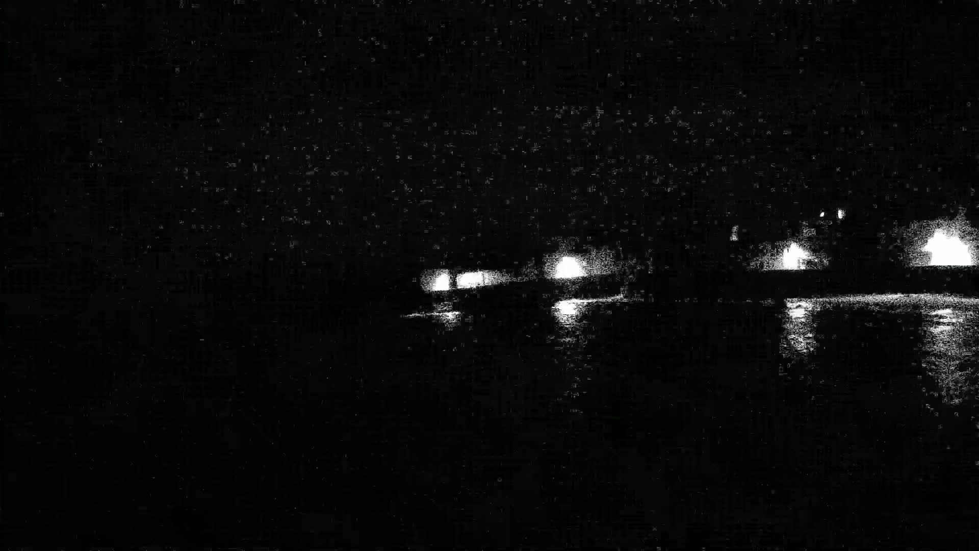 Distant lights reflect on dark water at night.